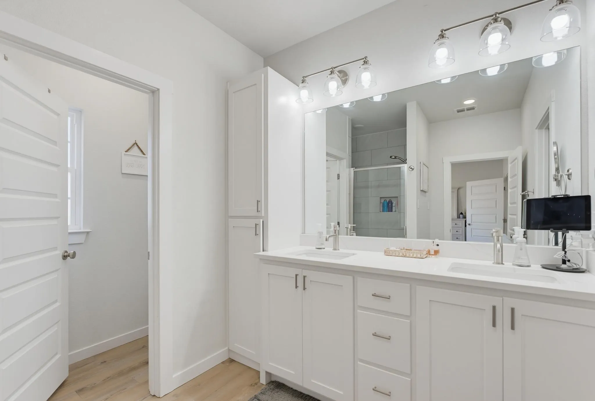 Dual vanity with undermount sinks, white cabinetry, a built-in linen tower, and a large wall-mounted mirror with overhead lighting