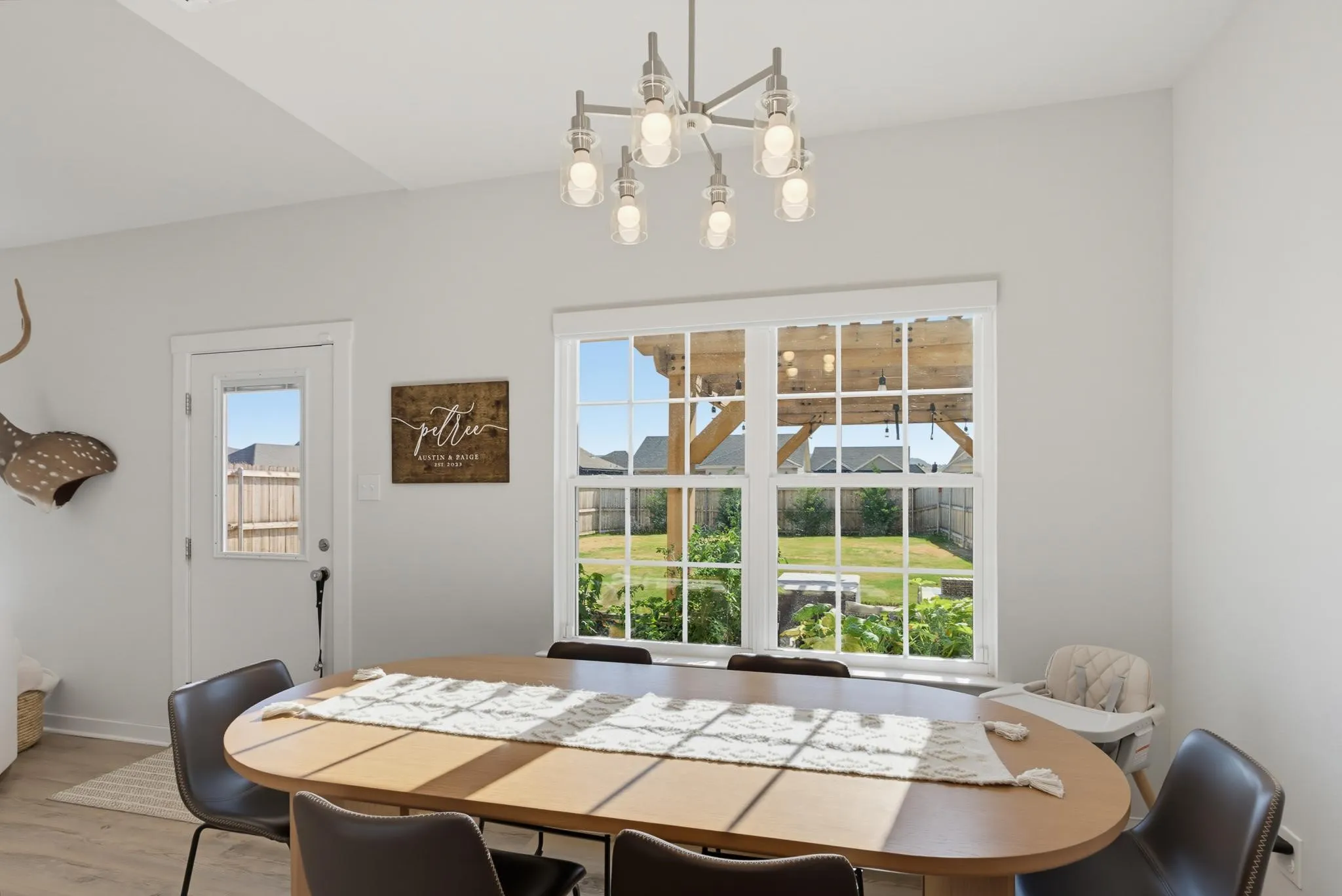 Wood-finish flooring, contemporary chandelier, and a bright window overlooking the backyard with a wooden pergola
