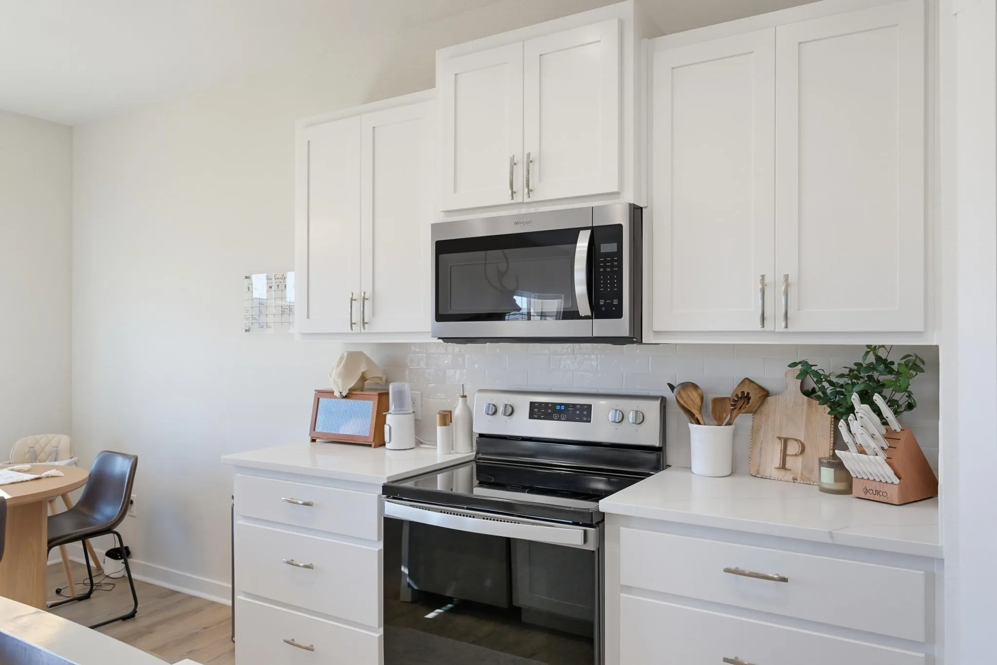White shaker-style cabinetry, stainless steel microwave, stainless steel electric range, subway tile backsplash, and light-toned countertops