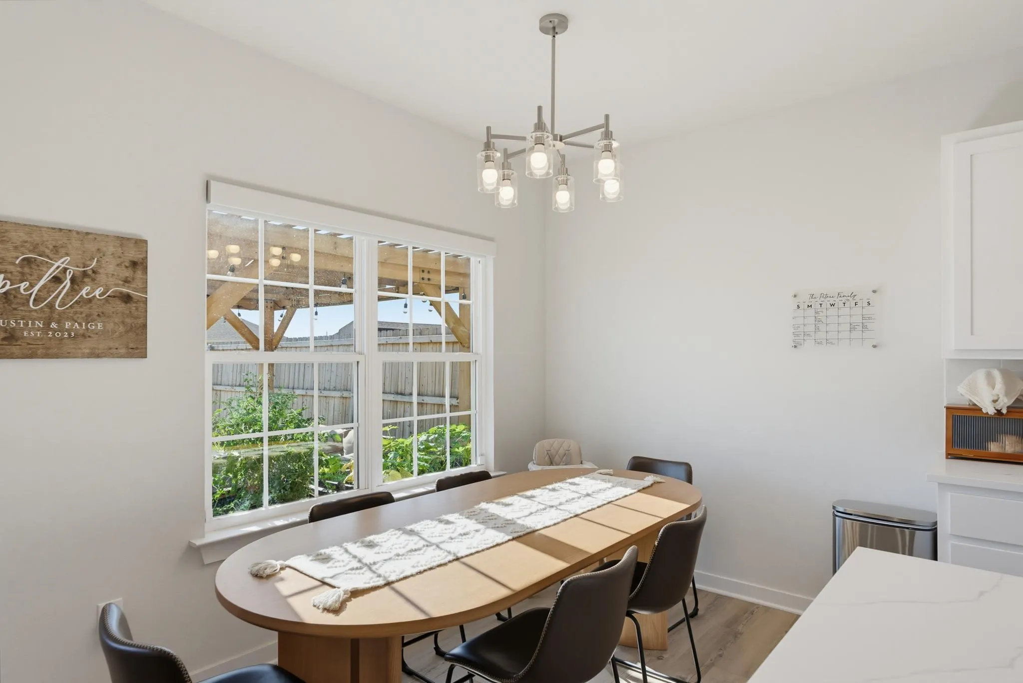 Spacious dining area featuring wood-finish flooring, a large window, a modern chandelier, and crisp white walls