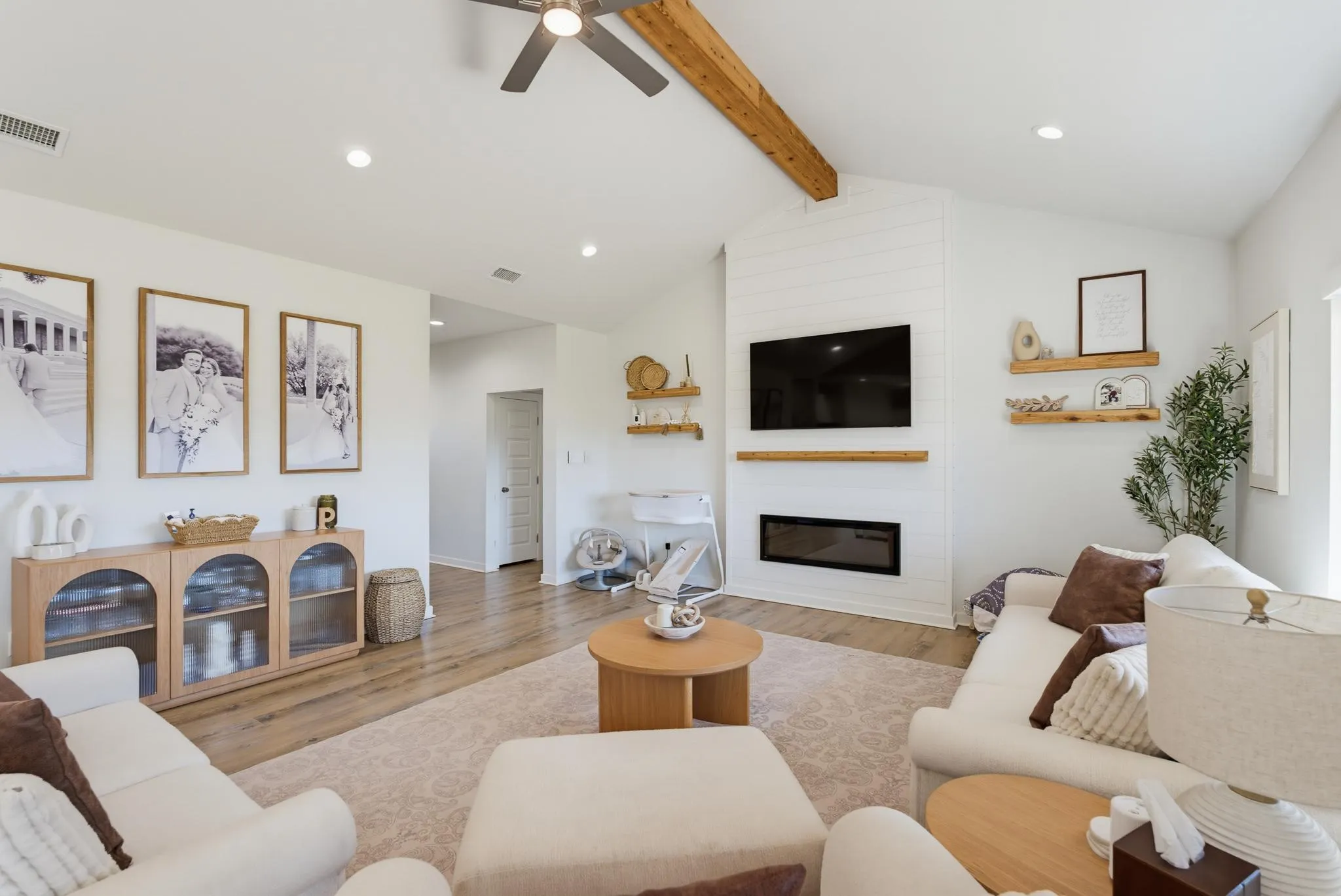 Vaulted ceiling with an exposed wood beam, recessed lighting, wood-finish flooring, shiplap-accented wall with an inset linear electric fireplace, and built-in wood shelving