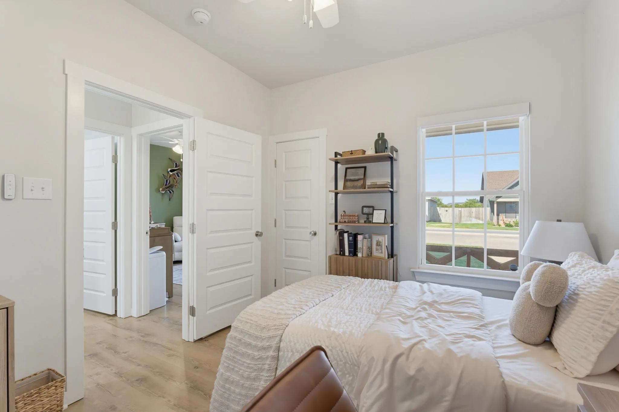 Light-toned wood-finish flooring, white paneled doors, a double-hung window, and a ceiling fan