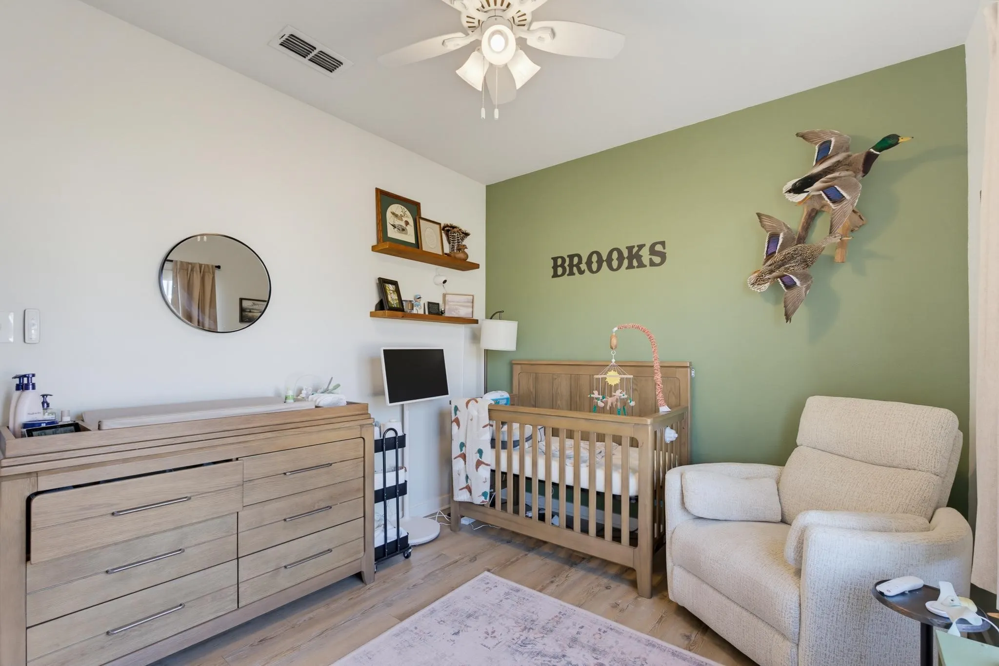 Wood-finish flooring with a light tone, wall-mounted shelving, and a ceiling fan with integrated lighting