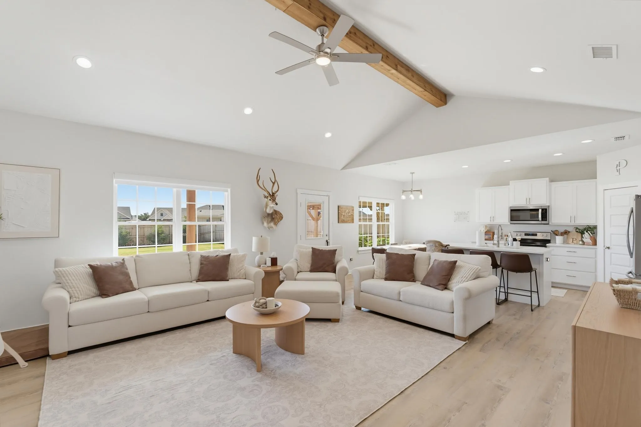 Vaulted ceiling with exposed wood beam, recessed lighting, wood-finish flooring, white cabinetry, and stainless steel appliances