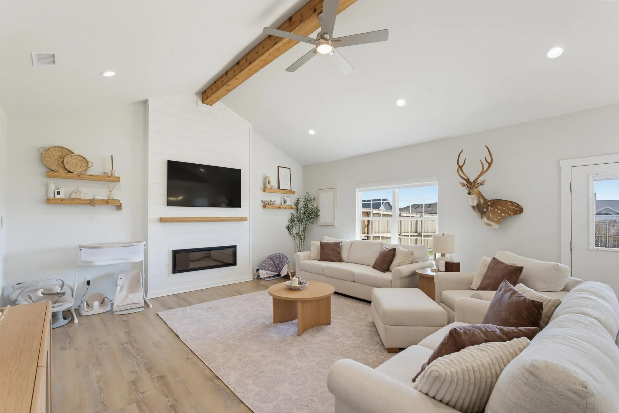 Vaulted ceiling with exposed wood beam, wood-finish flooring, recessed lighting, and a linear electric fireplace with shiplap surround