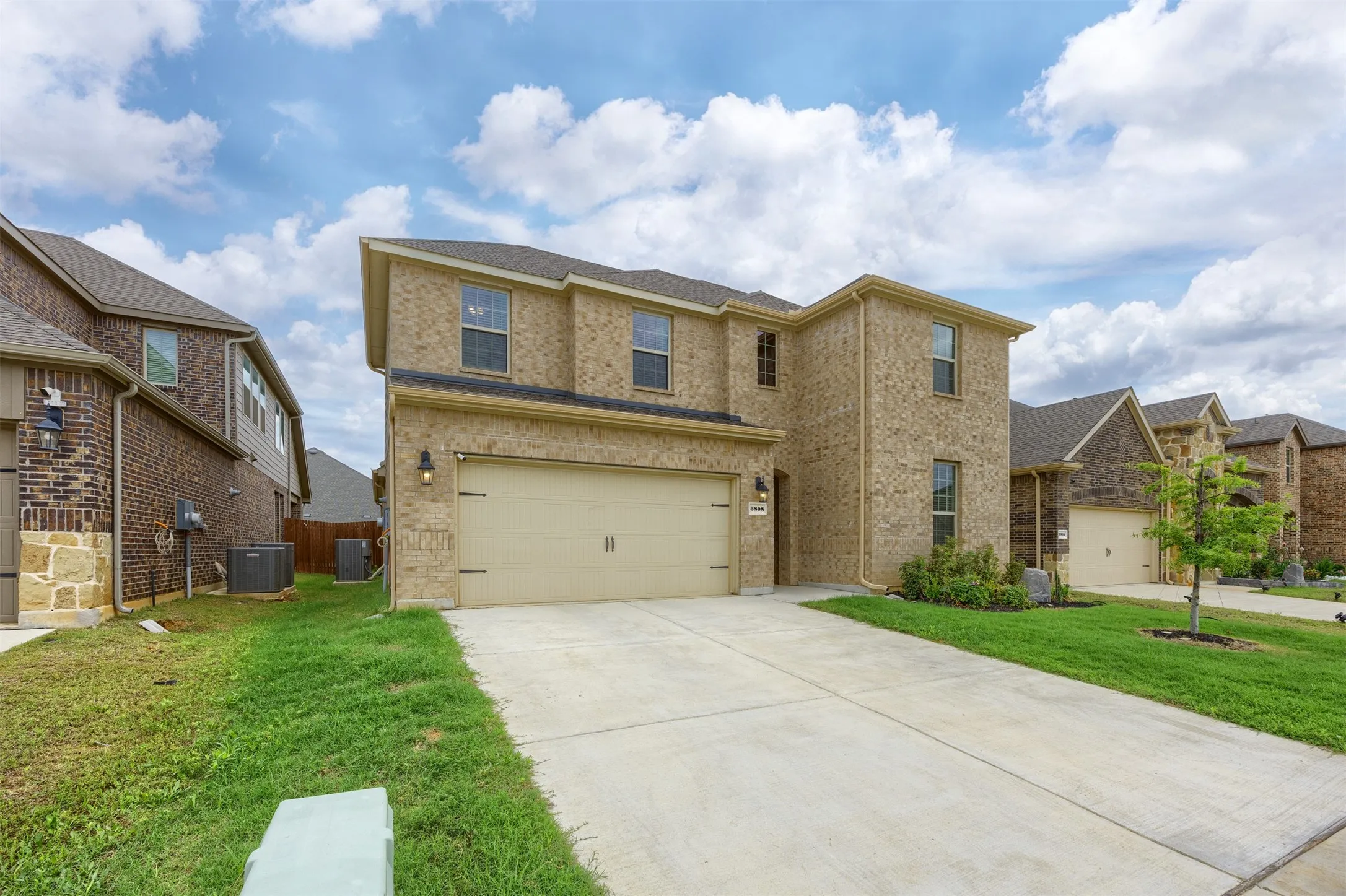 Two-story residence featuring a brick exterior, attached two-car garage, concrete driveway, and front landscaping