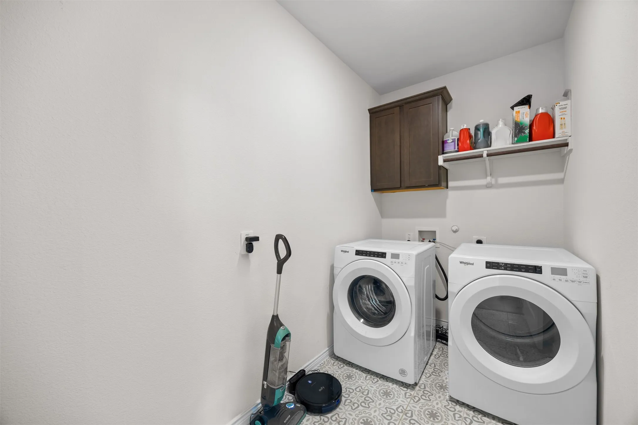 Laundry area featuring decorative floor tiling, an upper storage cabinet, and a wall-mounted shelf