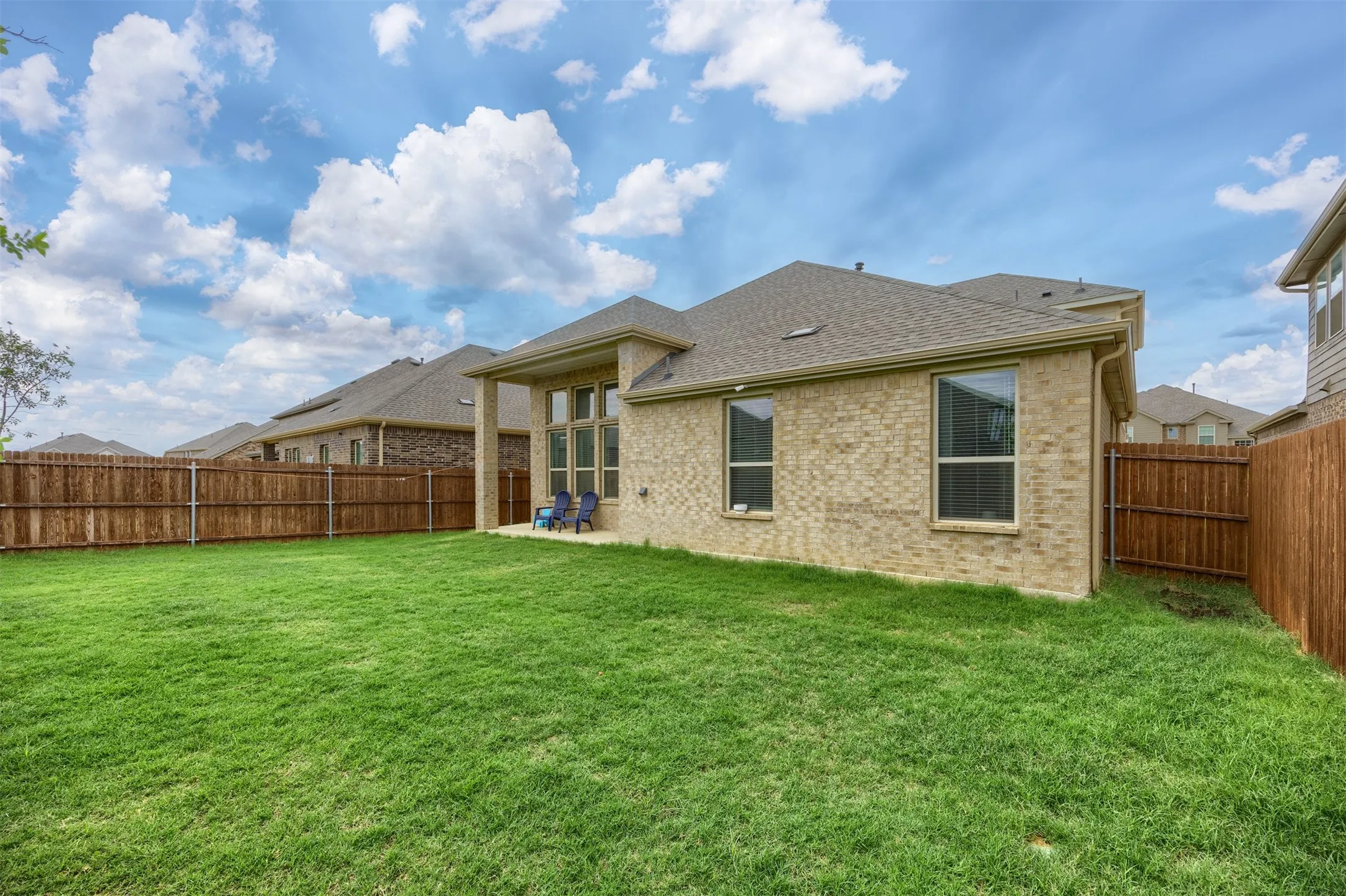 Expansive grassy yard with wood fencing, a covered patio, and a brick exterior