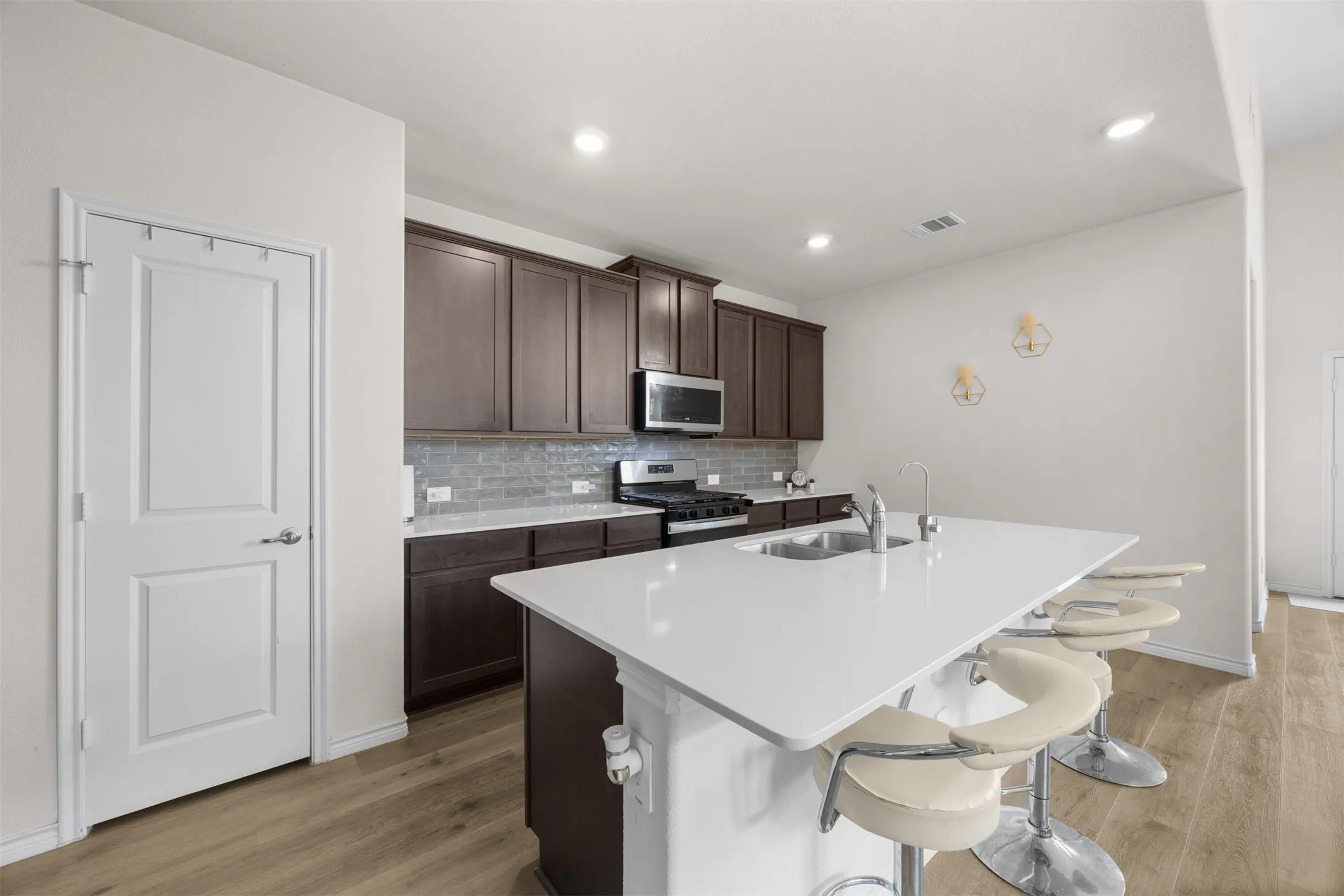 Kitchen featuring an expansive island with an undermount sink, dark wood-finish cabinetry, a subway tile backsplash, and wood-finish flooring