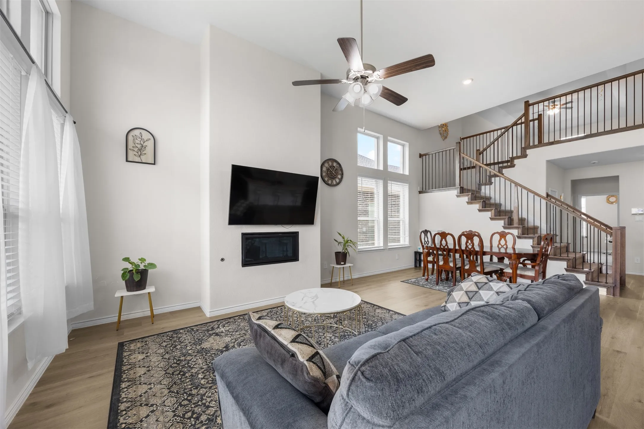Vaulted ceilings with a ceiling fan, a built-in fireplace, wood-finish flooring, and a staircase with dark wood railings and black balusters