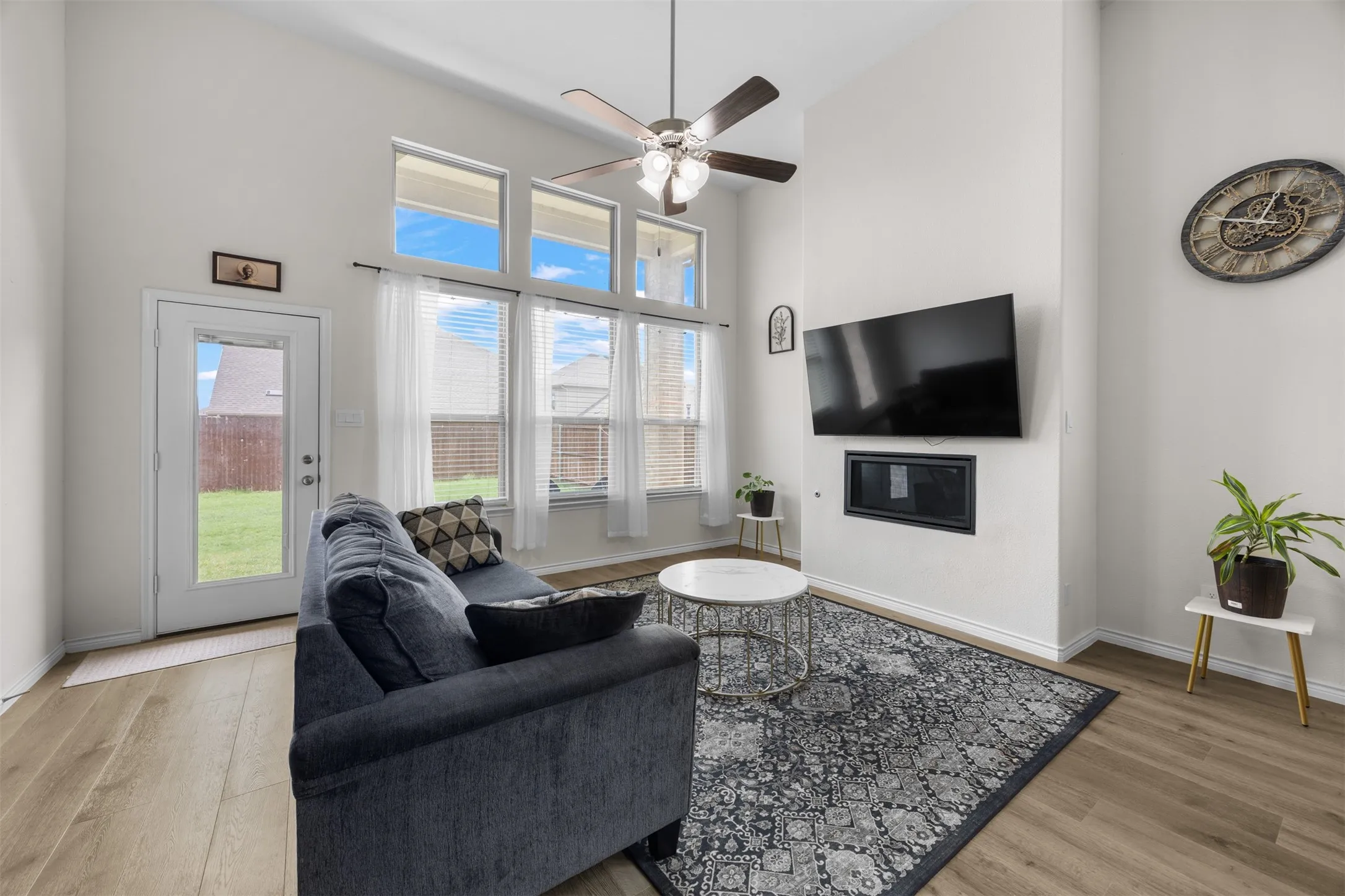 Vaulted ceiling with a ceiling fan, wood-finish flooring, multiple windows providing ample light, and a built-in fireplace feature