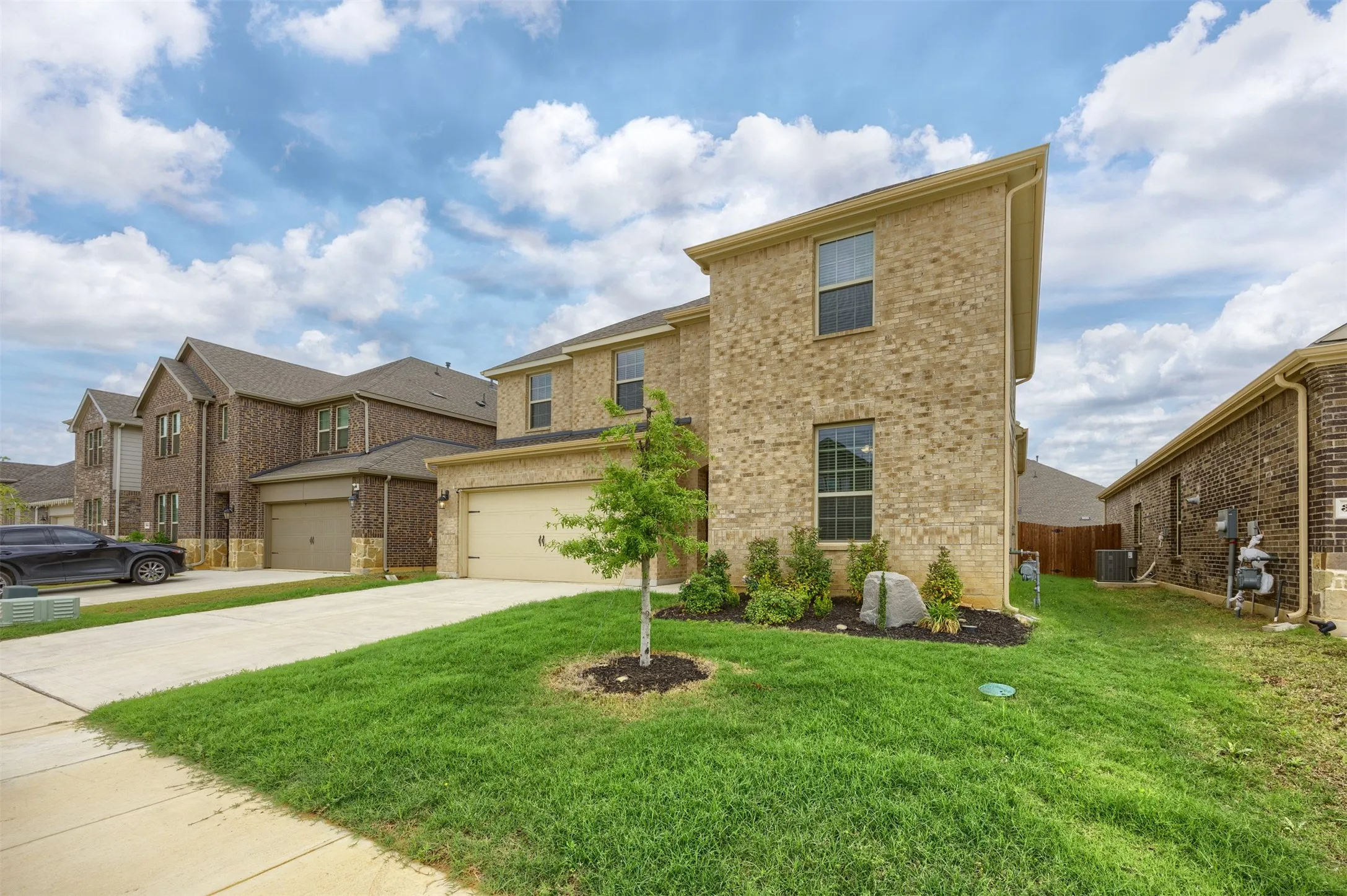 Two-story brick exterior with a two-car garage, concrete driveway, and front lawn landscaping
