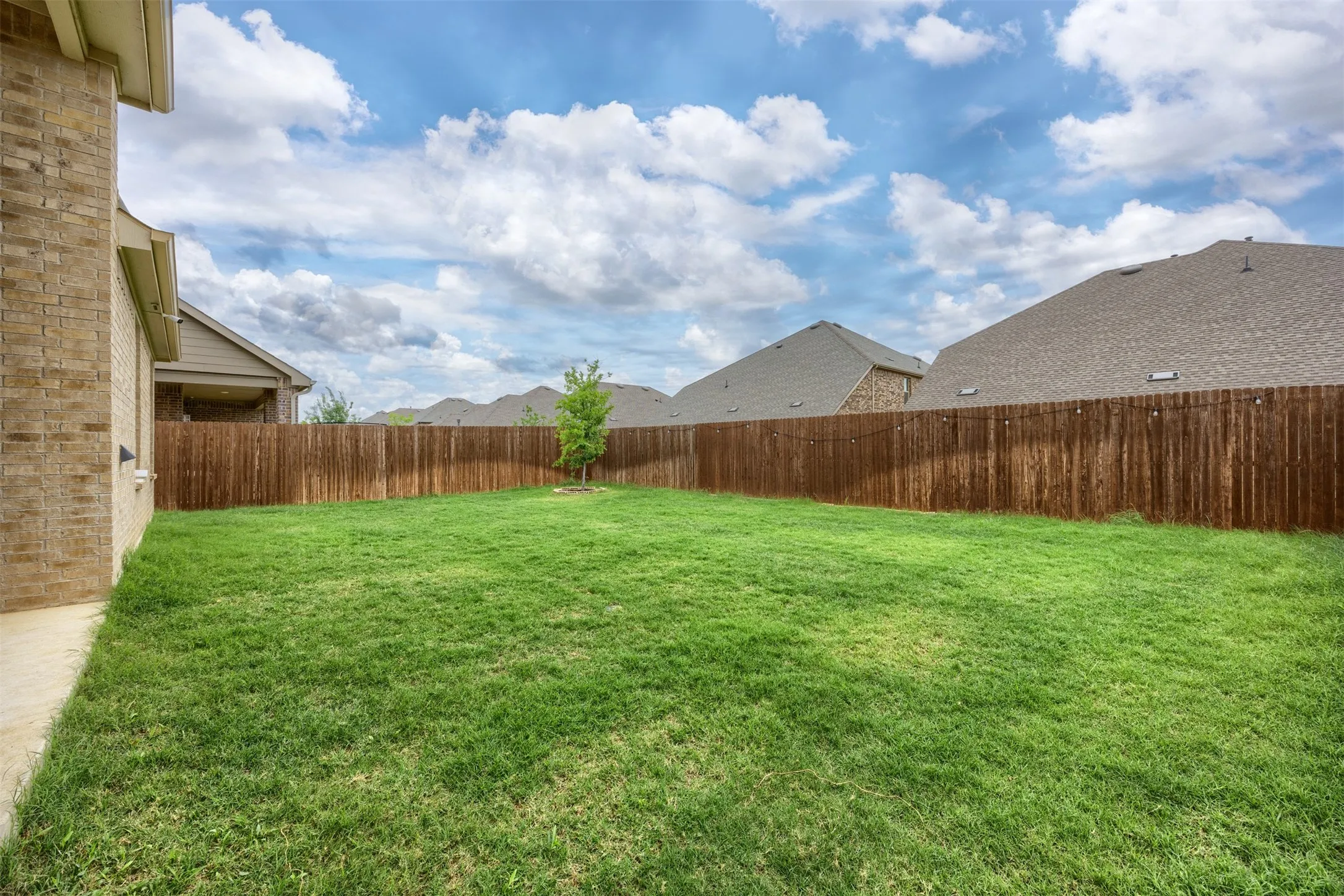 Expansive backyard featuring a manicured lawn, full privacy fencing, and a brick exterior
