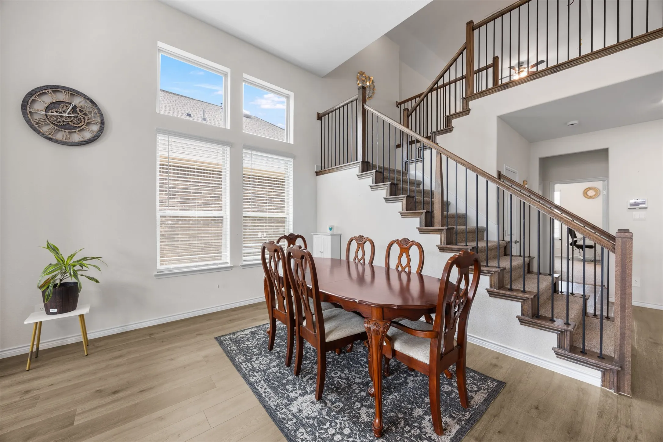 Two-story ceiling, large multi-pane windows, wood-finish flooring, staircase with dark wood-finish banister, and wrought iron balusters