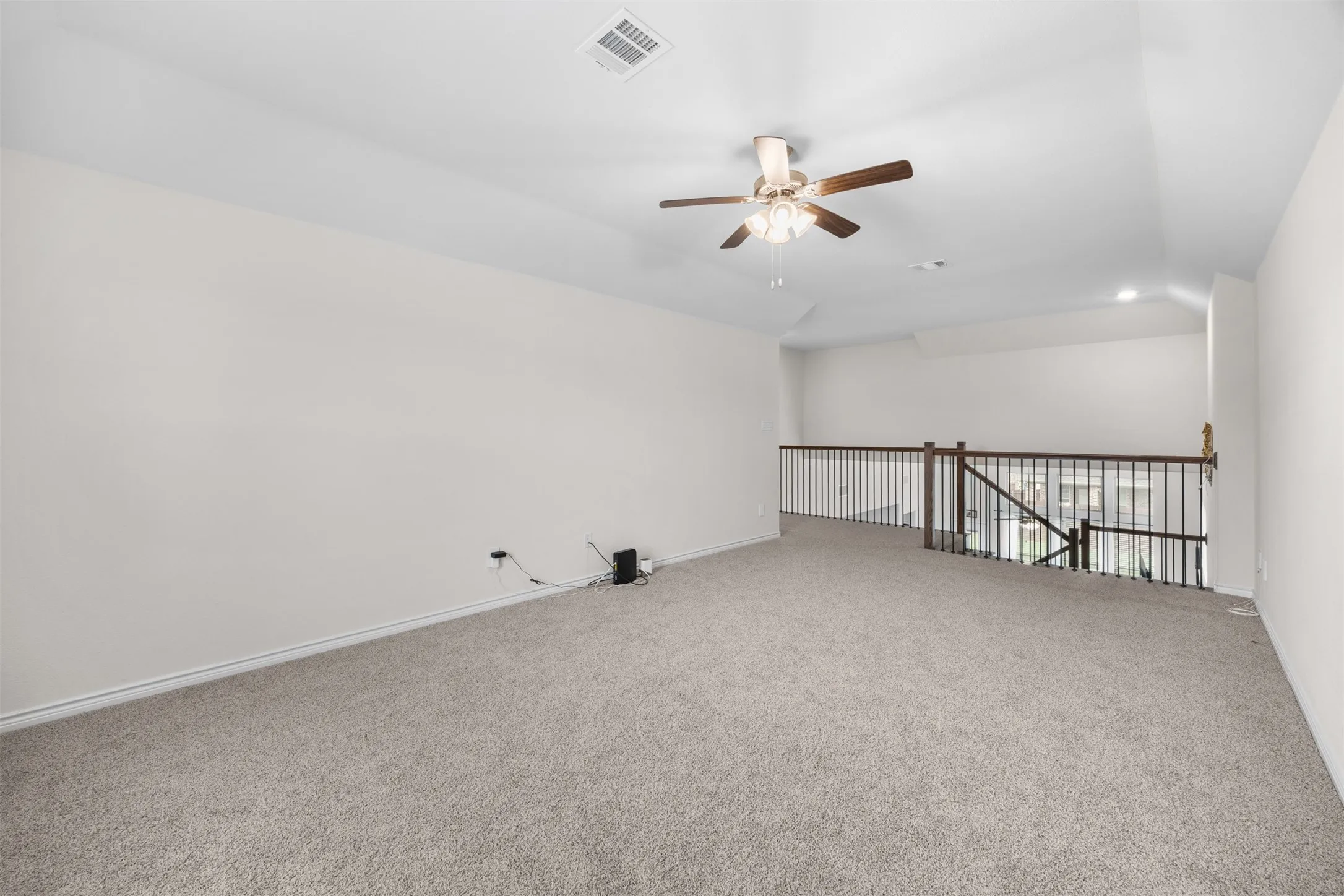 Carpeted upper-level space with a vaulted ceiling, ceiling fan, and spindle railing overlooking the level below