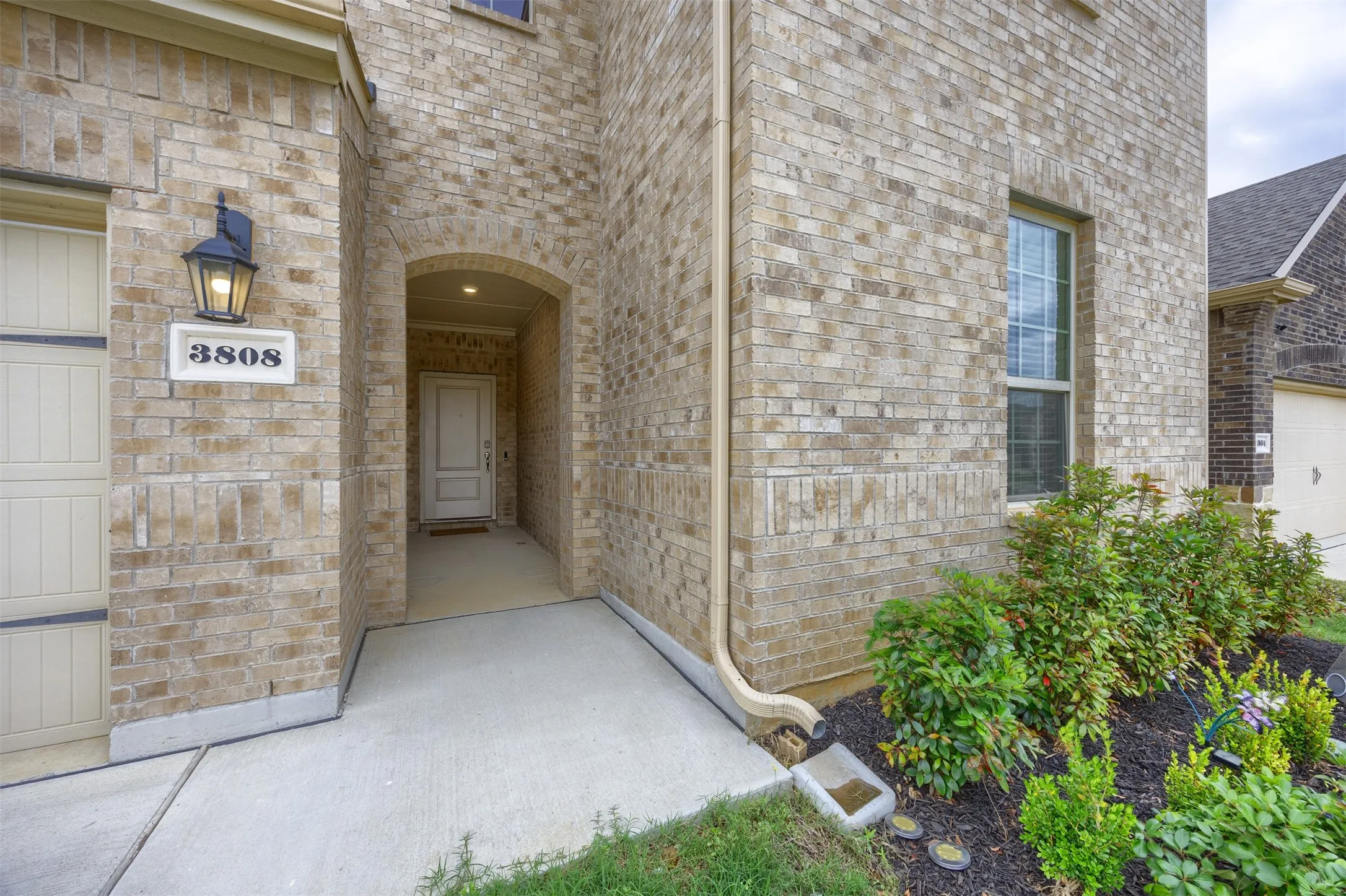 Brick facade with an arched entry, prominent house numbers, and a decorative exterior light fixture