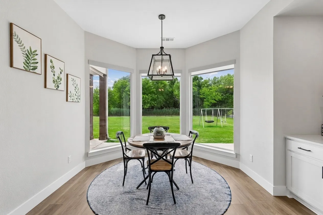 Bay window dining area with wood-finish LVP flooring, a modern geometric light fixture, and white cabinetry