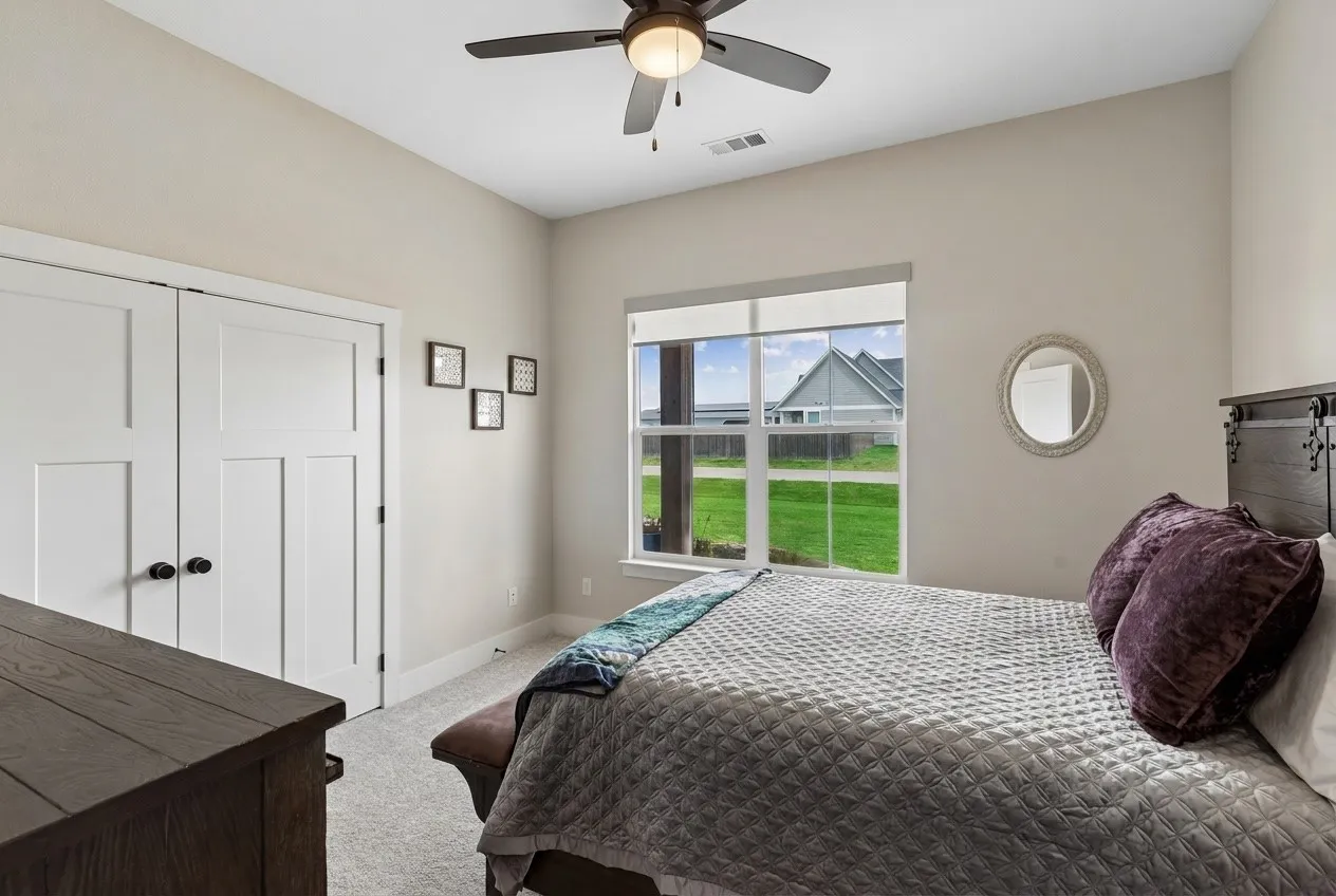 Recessed ceiling with ceiling fan, large window with roller shade, neutral wall tones, paneled closet doors with dark hardware, and carpet flooring