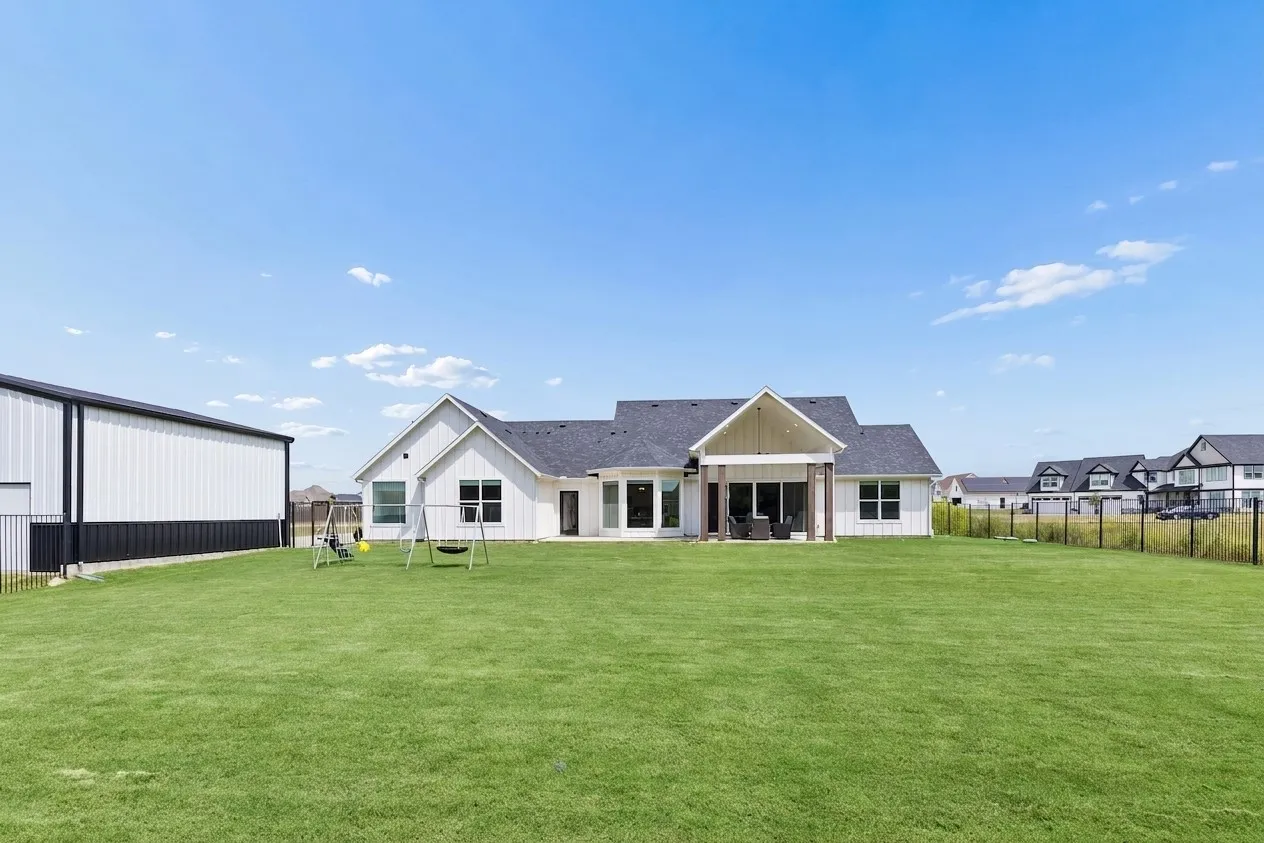 Expansive grassy lawn with a covered patio, a detached RV garage, and a black metal fence