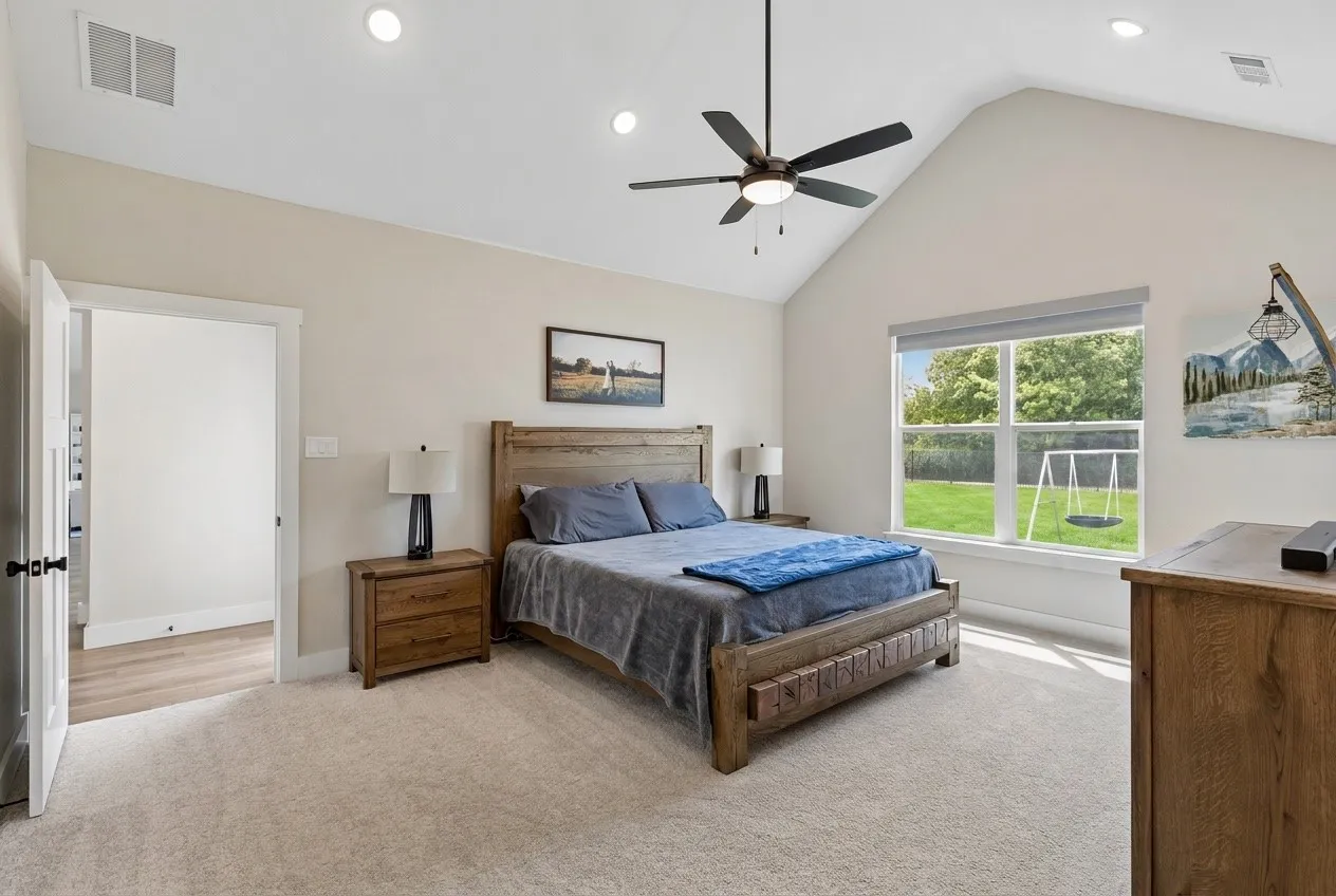 Vaulted ceiling with recessed lighting and ceiling fan, large window overlooking a manicured lawn, and plush carpeting
