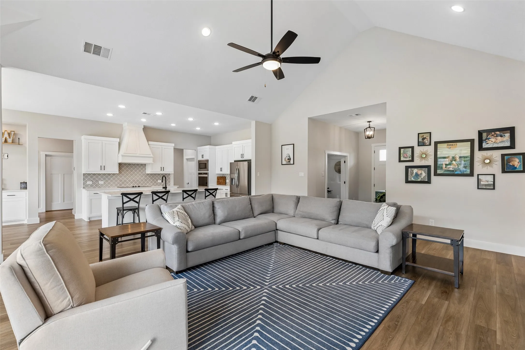 Vaulted ceiling with a ceiling fan and recessed lighting, wood-finish LVP flooring, and an open-concept kitchen featuring white cabinetry, a tile backsplash, and a kitchen island with bar seating