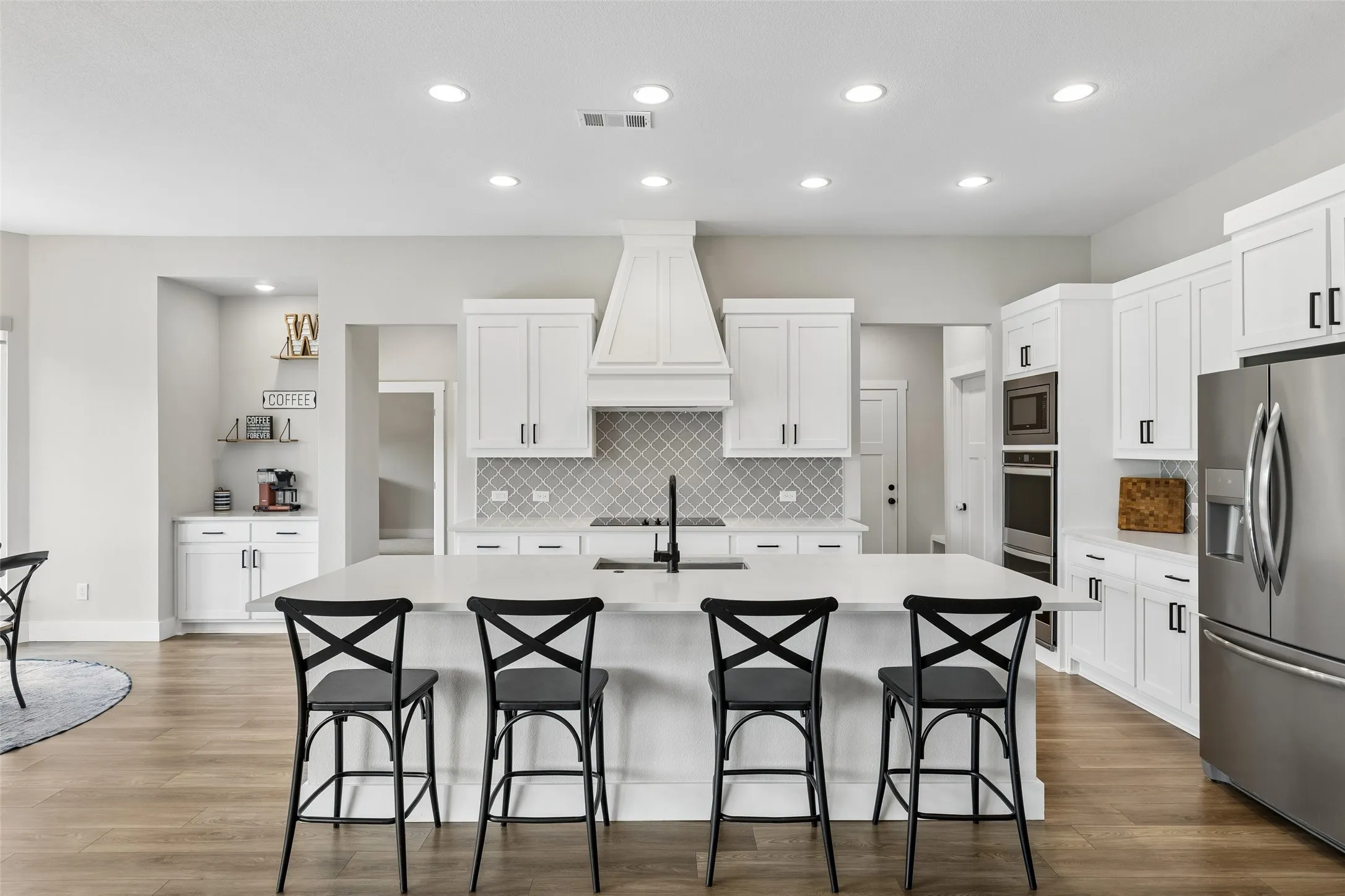 Open-concept kitchen with recessed lighting, a large island with seating, stainless steel appliances, and wood-finish LVP flooring