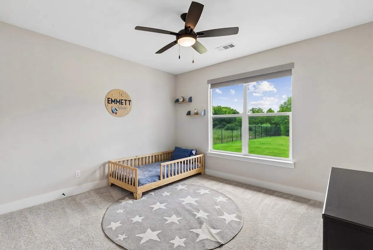 Carpeted room featuring a ceiling fan, a large window with roller shade