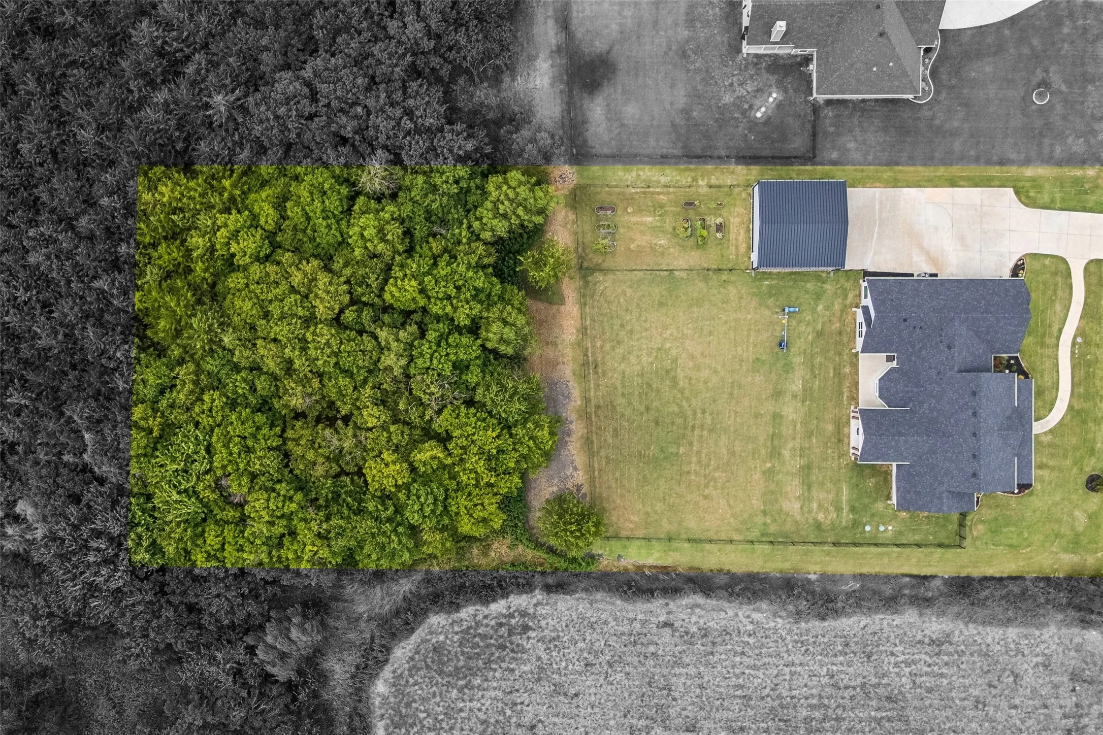 Expansive green lot featuring approximately one-quarter acre of wooded property to ensure long-term privacy, a residential structure with a dark roof, a detached RV garage, and a cement driveway.