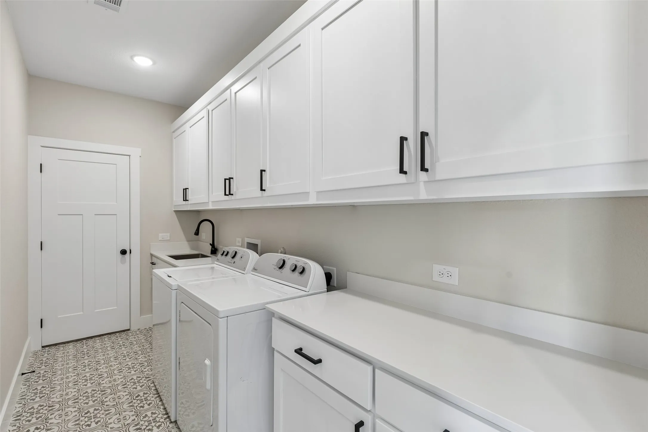 White shaker cabinetry, dark hardware accents, light-toned countertops, integrated sink, and patterned floor tile