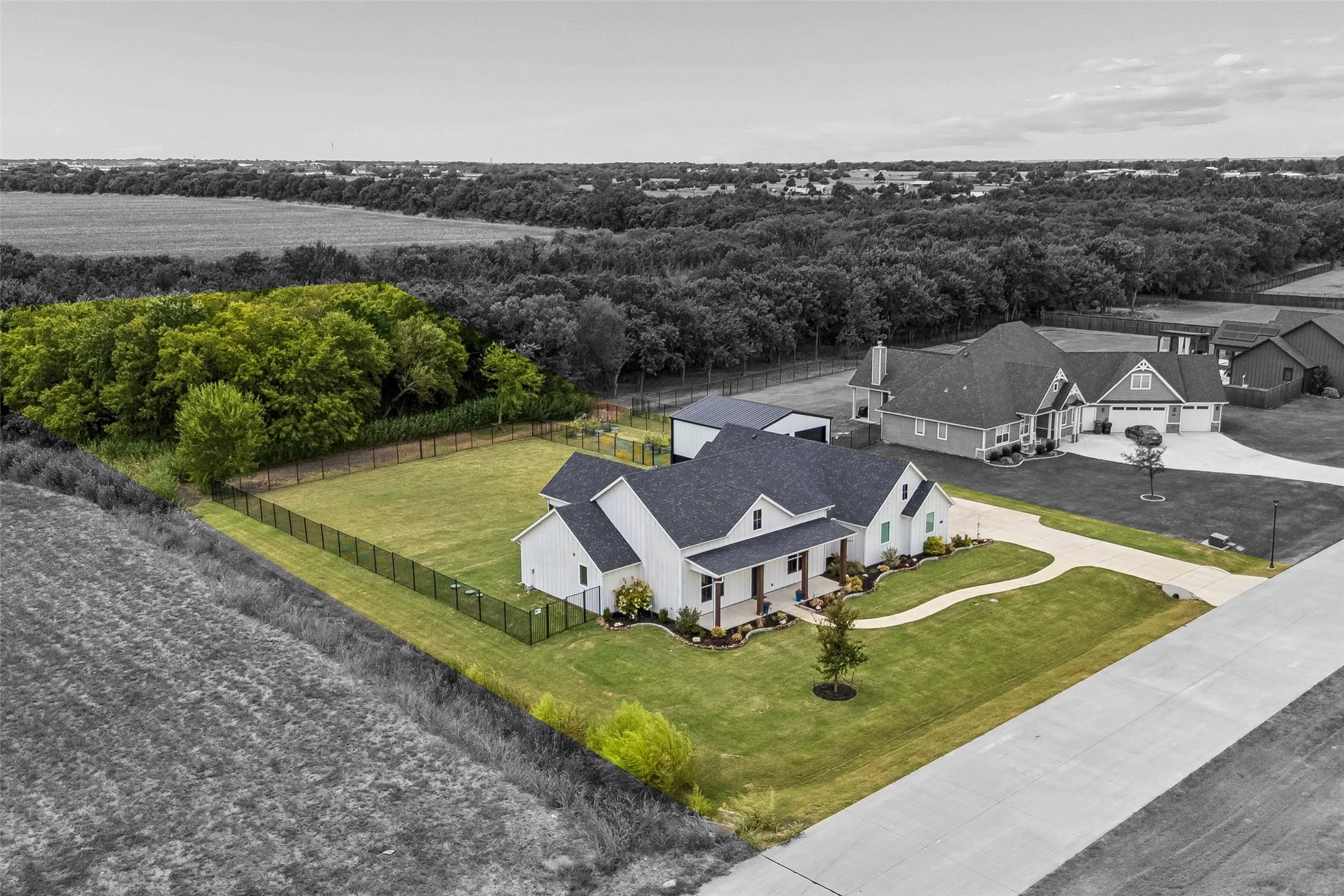 White siding exterior with a dark shingle roof, a covered front porch, and a detached RV garage. Approximately one-quarter acre of wooded property to ensure long-term privacy.