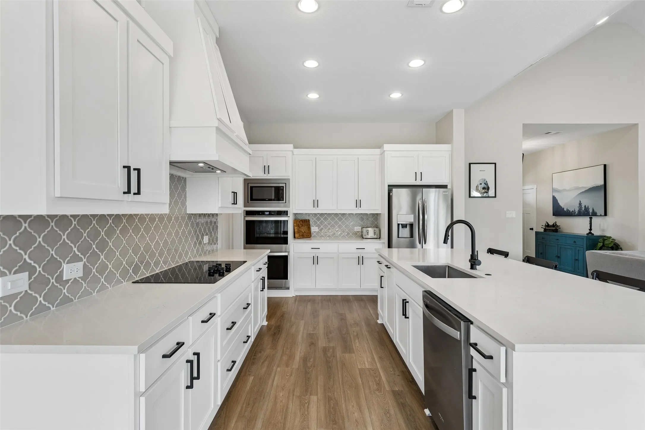 Kitchen featuring white cabinetry, light-toned countertops, a mosaic tile backsplash, stainless steel appliances, and wood-finish LVP flooring