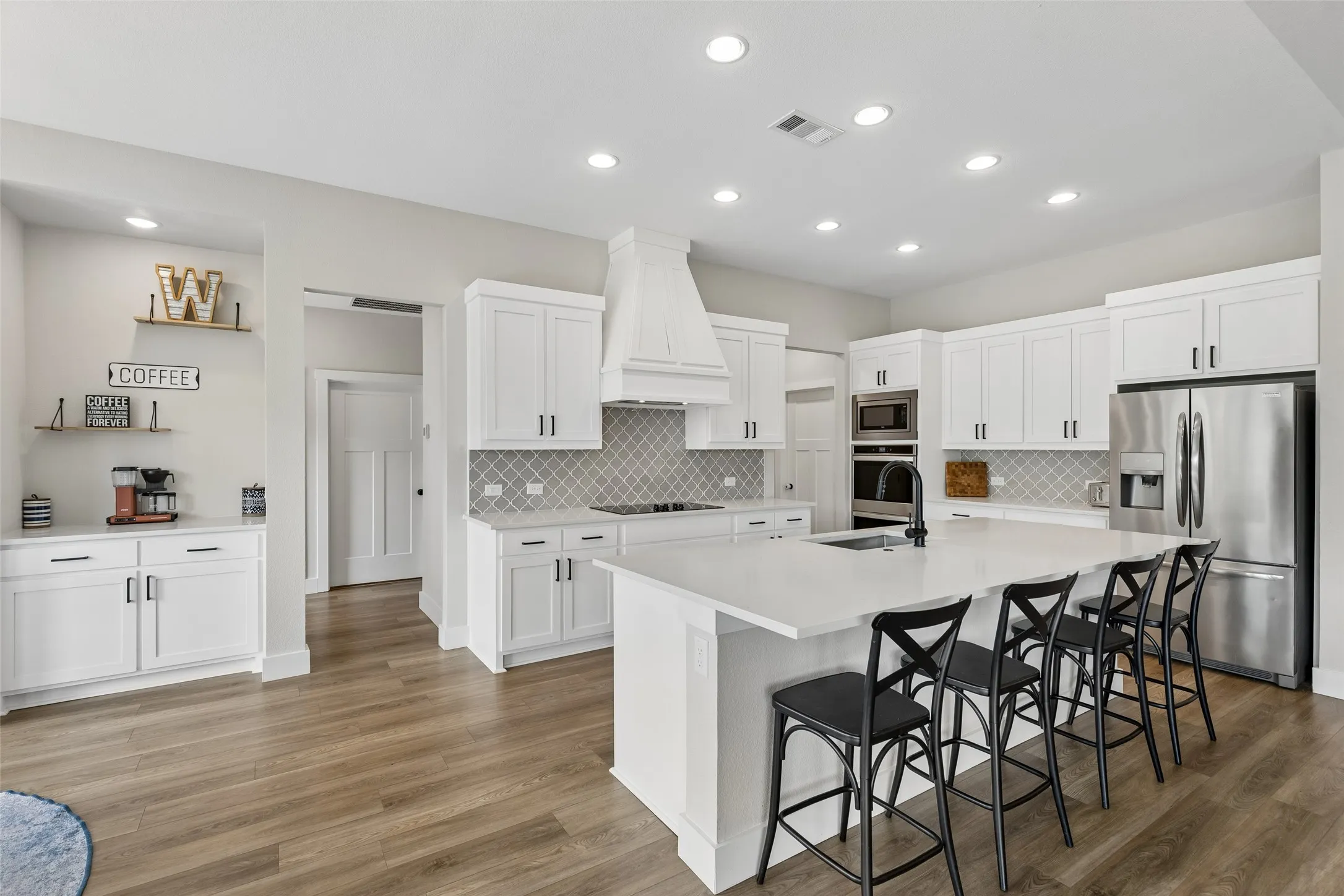 Spacious kitchen featuring an expansive island, white cabinetry, integrated stainless steel appliances, a stylish tile backsplash, and wood-finish LVP flooring