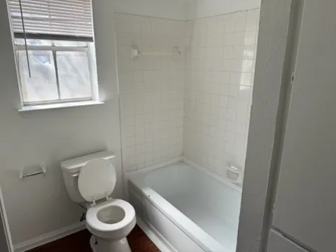 Bathroom featuring baseboards, toilet, shower / bath combination, and wood finished floors