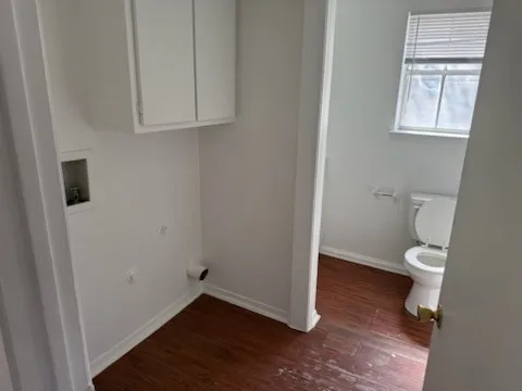Laundry area featuring washer hookup, baseboards, laundry area, and wood finished floors. Located in the bath
