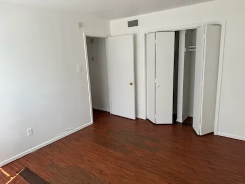 Unfurnished bedroom featuring baseboards, dark wood-style floors, visible vents, and a closet