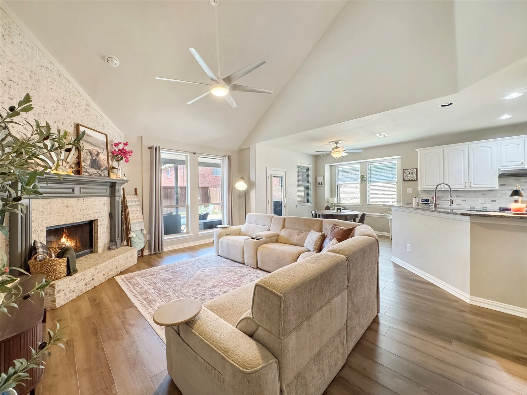 Living area featuring vaulted ceilings, wood-finish flooring, a brick fireplace with mantel, and large windows overlooking a backyard pool