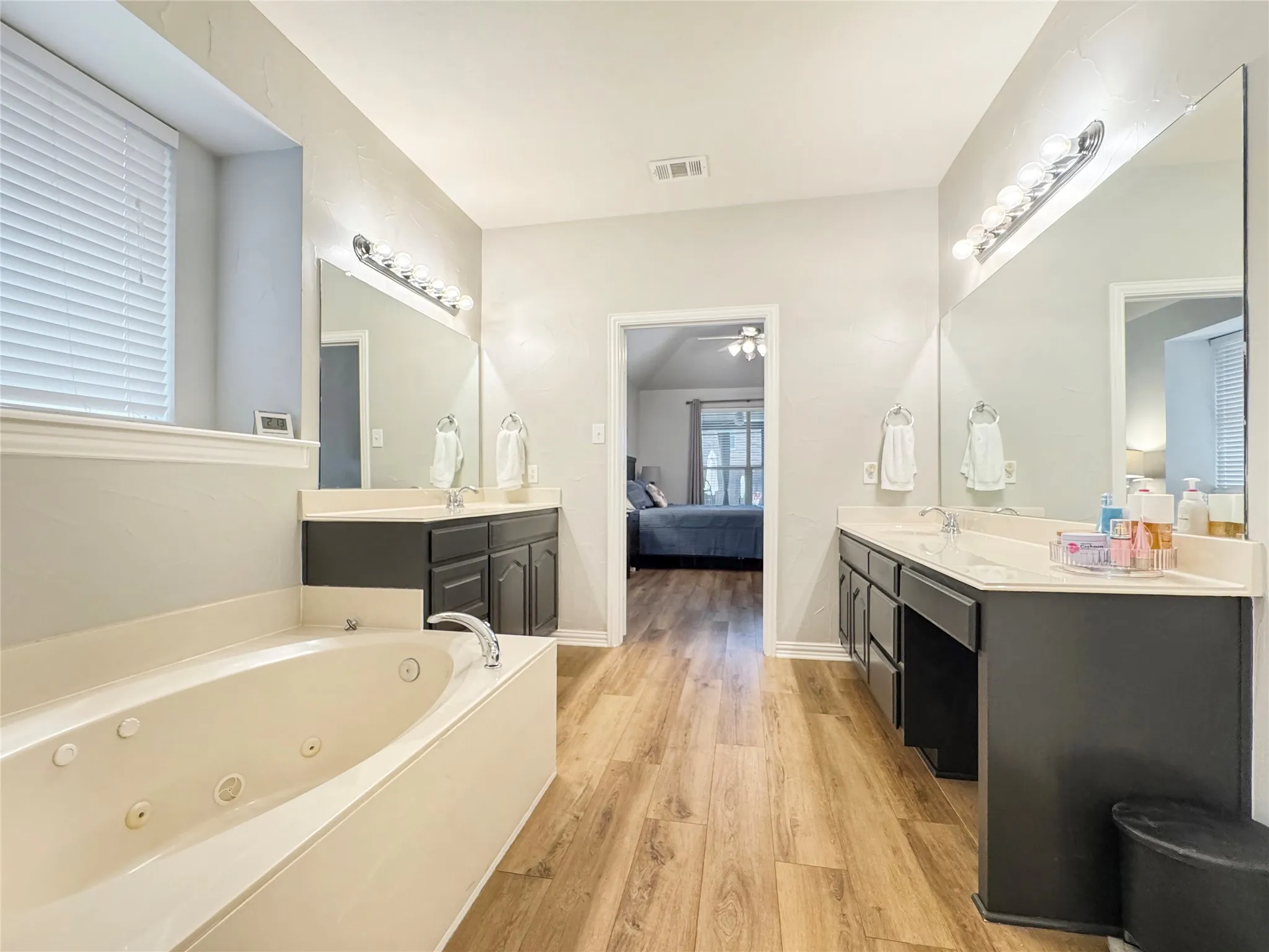 Dual vanities with white countertops, wood-finish flooring, a built-in jetted soaking tub, and a separate glass-enclosed shower