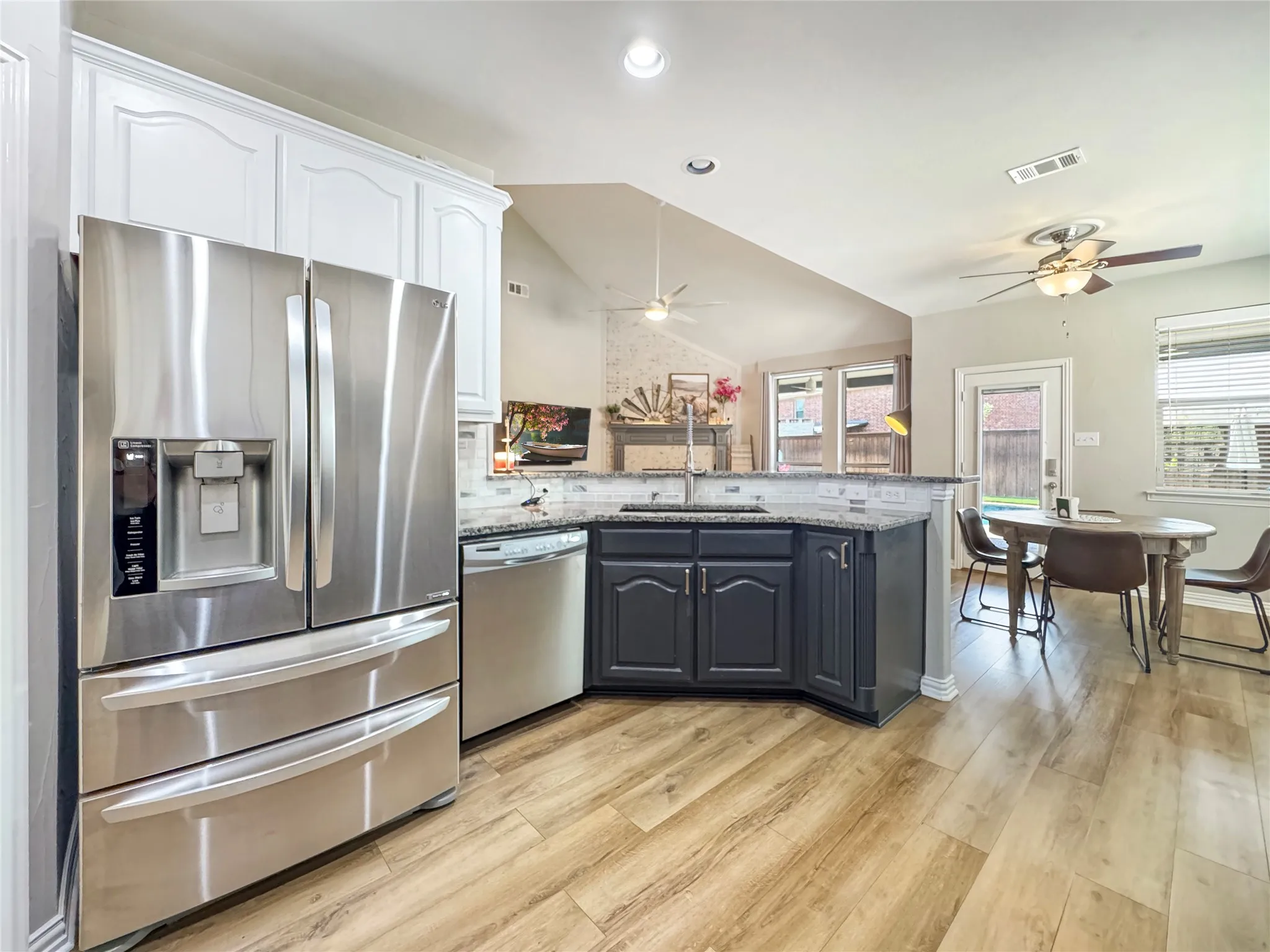 Two-tone cabinetry with contrasting finishes, a tile backsplash, stainless steel appliances, and wood-finish flooring