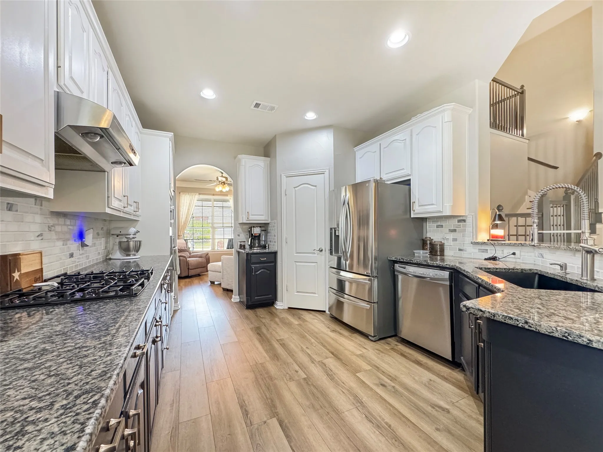Spacious kitchen featuring stainless steel appliances, wood-finish flooring, white upper cabinetry, dark lower cabinetry, and a granite countertop