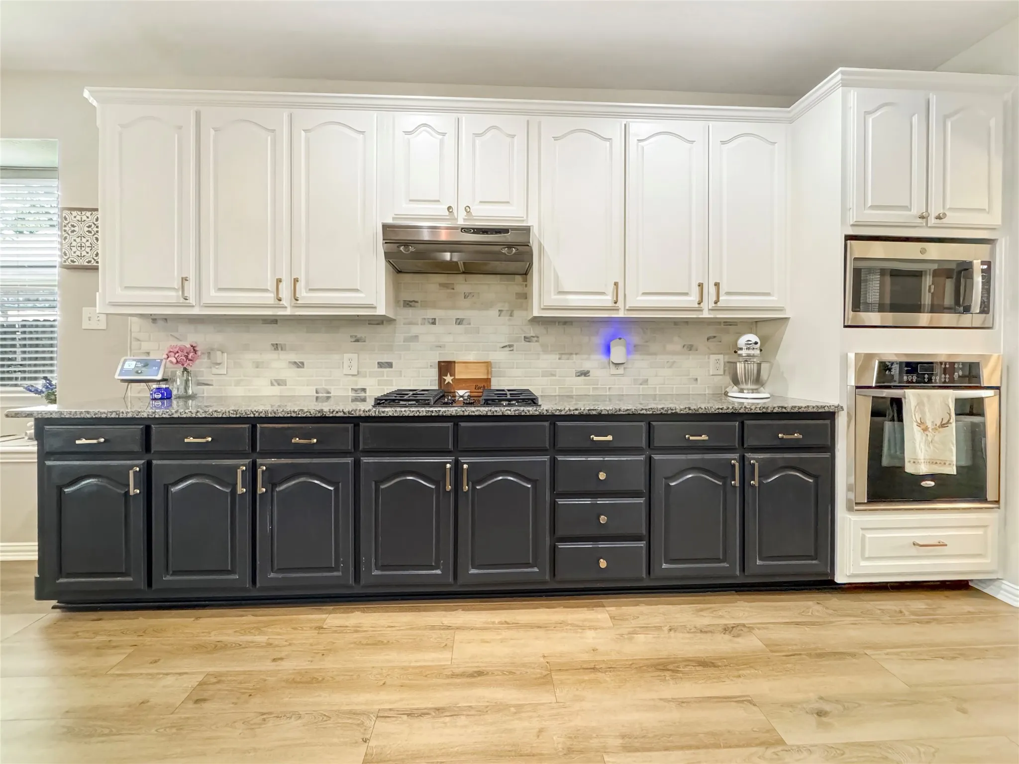 Kitchen featuring wood-finish flooring, two-tone cabinetry, granite countertops, and stainless steel appliances