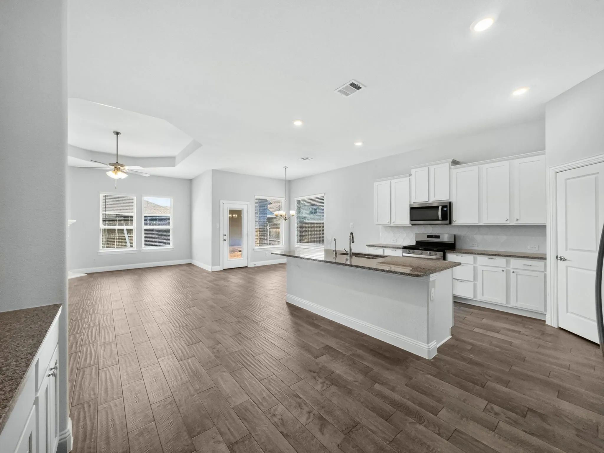 Open-concept living area featuring wood-finish flooring, a tray ceiling, and a ceiling fan