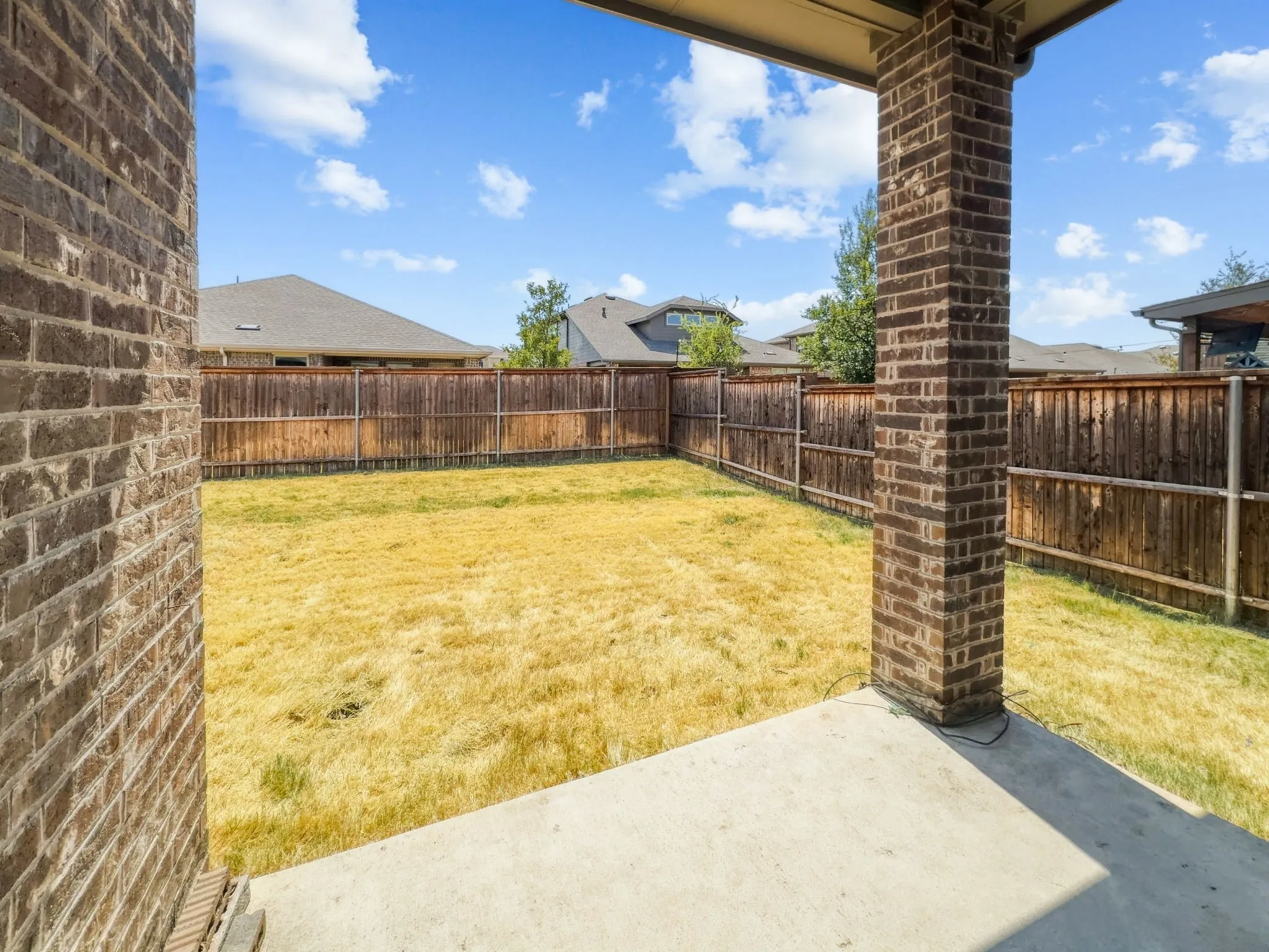 Covered patio with a concrete slab, brick support columns, and a fenced backyard