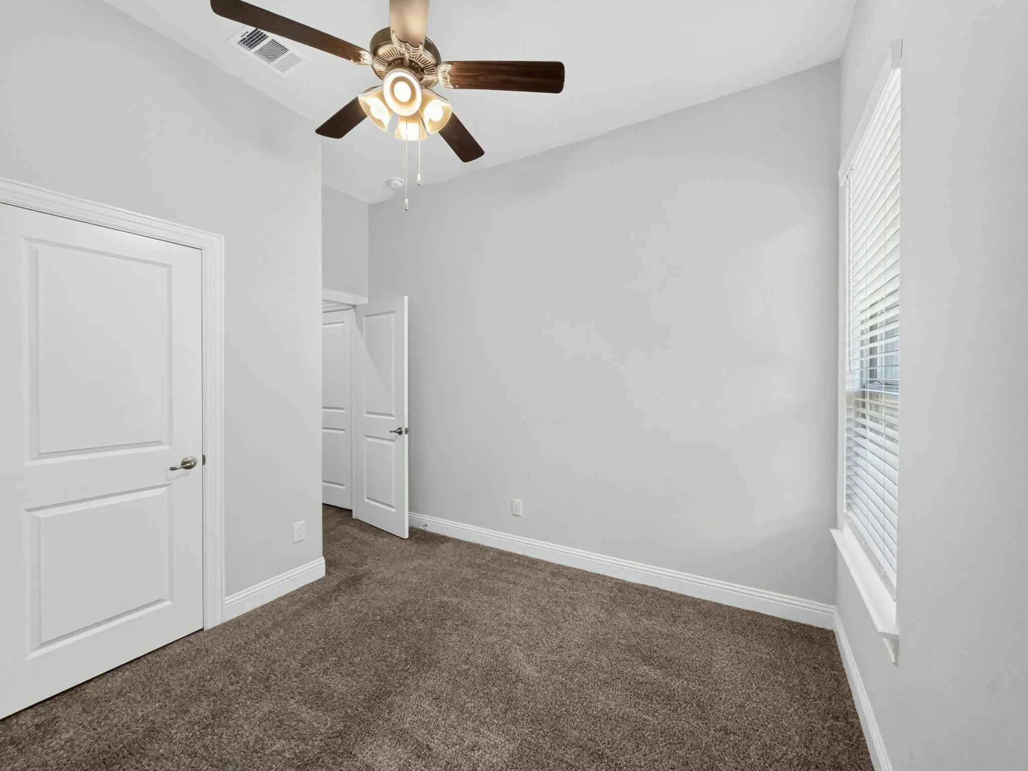 Carpeted room featuring a ceiling fan with integrated lighting, white paneled doors, and a window with blinds
