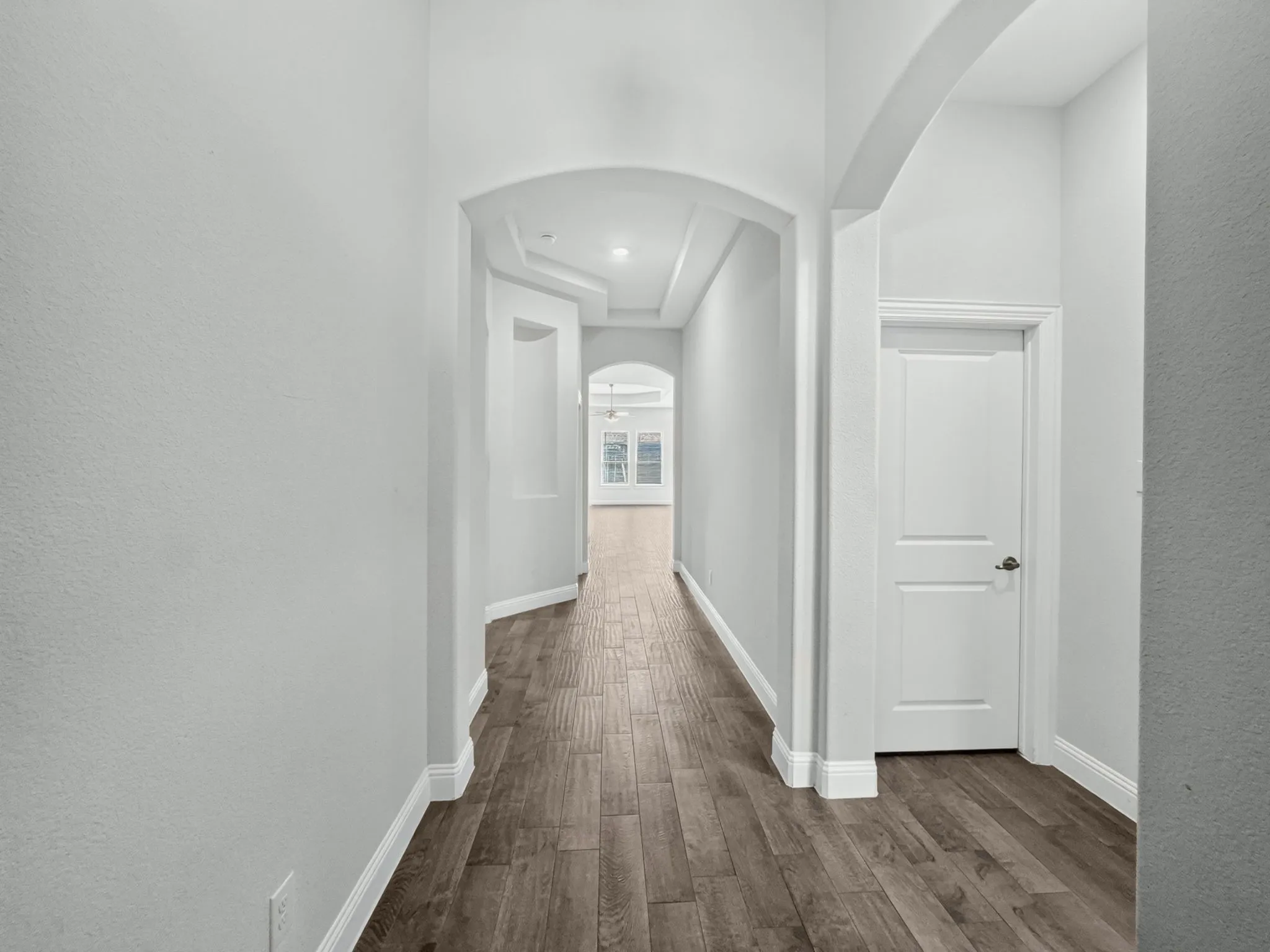 Hallway with wood-finish flooring, light gray walls, and arched doorways