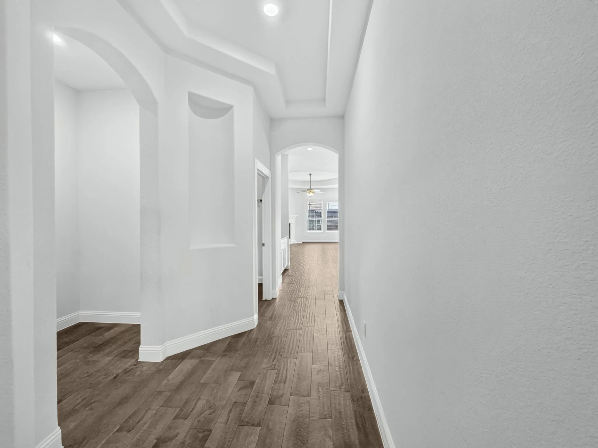 Hallway featuring wood-finish flooring, recessed lighting, arched doorways, a tray ceiling, and an architectural wall niche