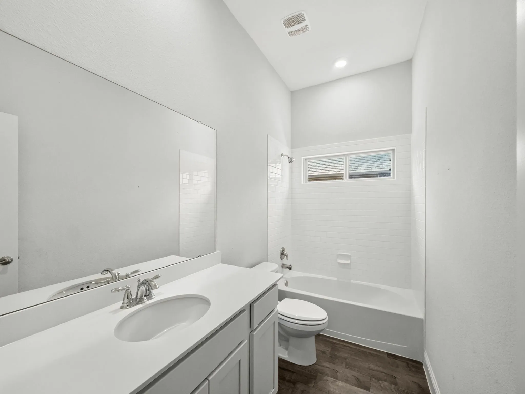 Vanity with an integrated sink and chrome faucet, large frameless mirror, subway tile shower surround, and wood-finish flooring