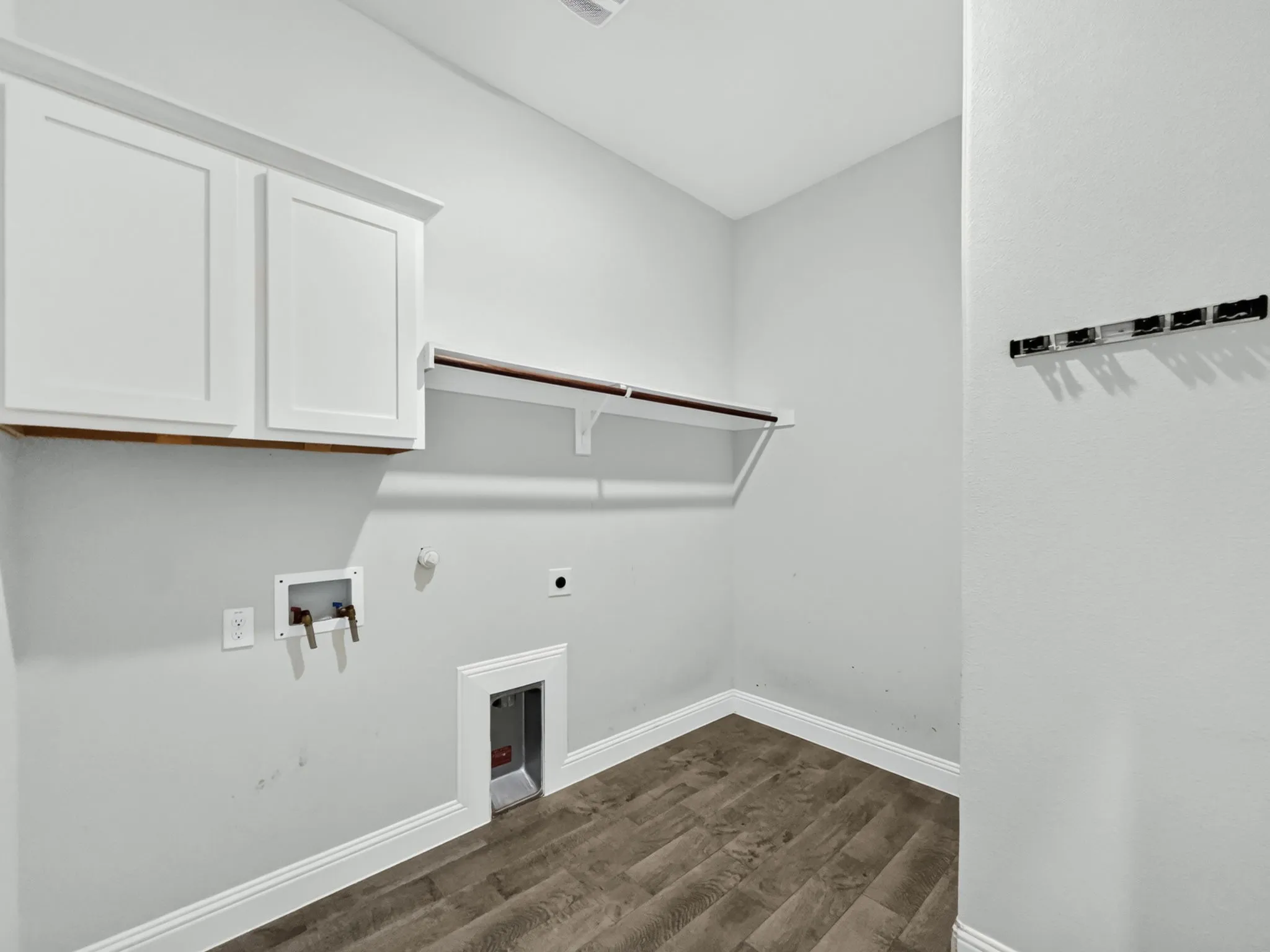 Wood-finish flooring with white trim, white upper cabinetry, and a wall-mounted shelving unit