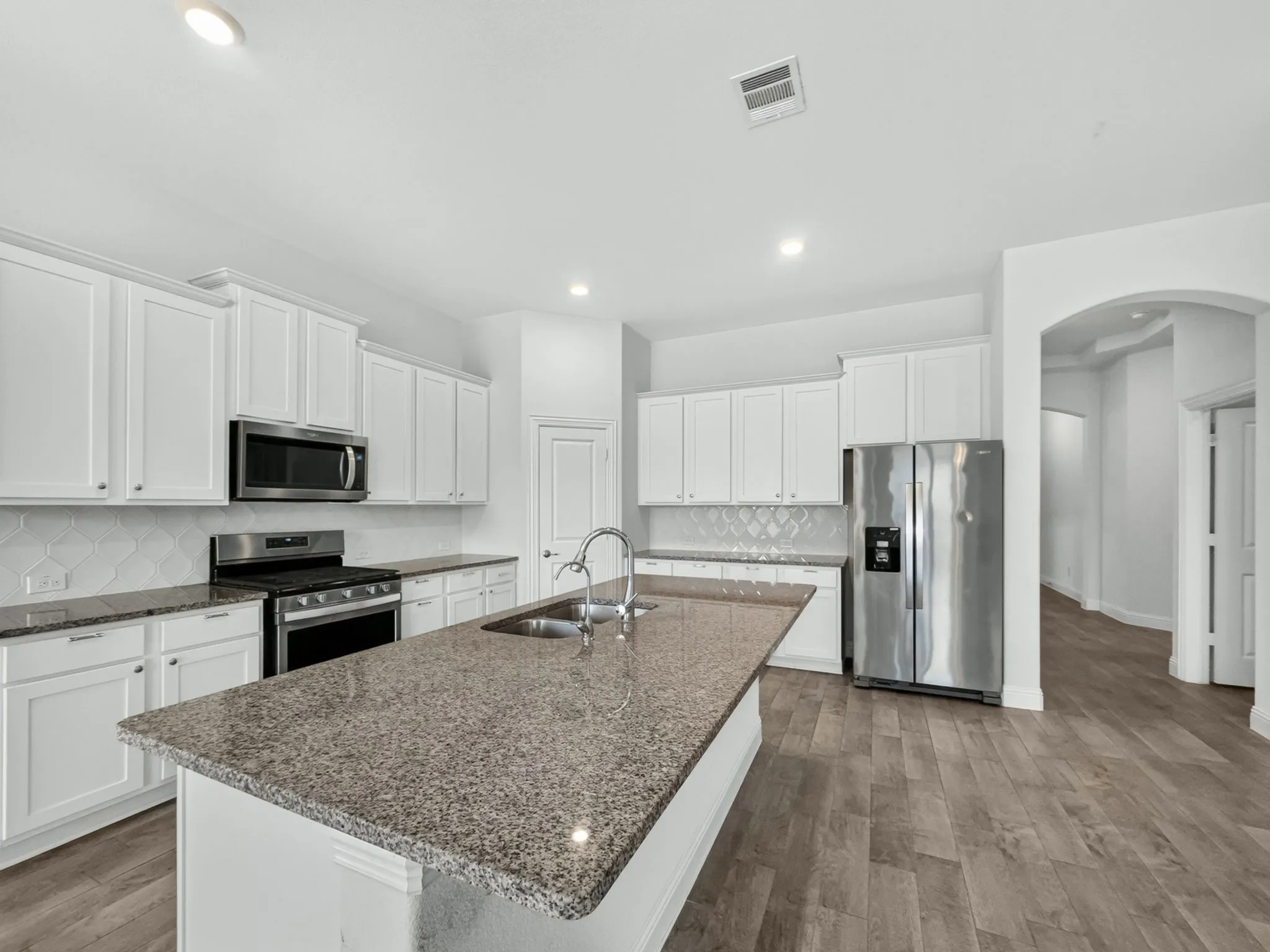 Kitchen featuring white cabinetry, stainless steel appliances, granite countertops, a tile backsplash, and wood-finish flooring