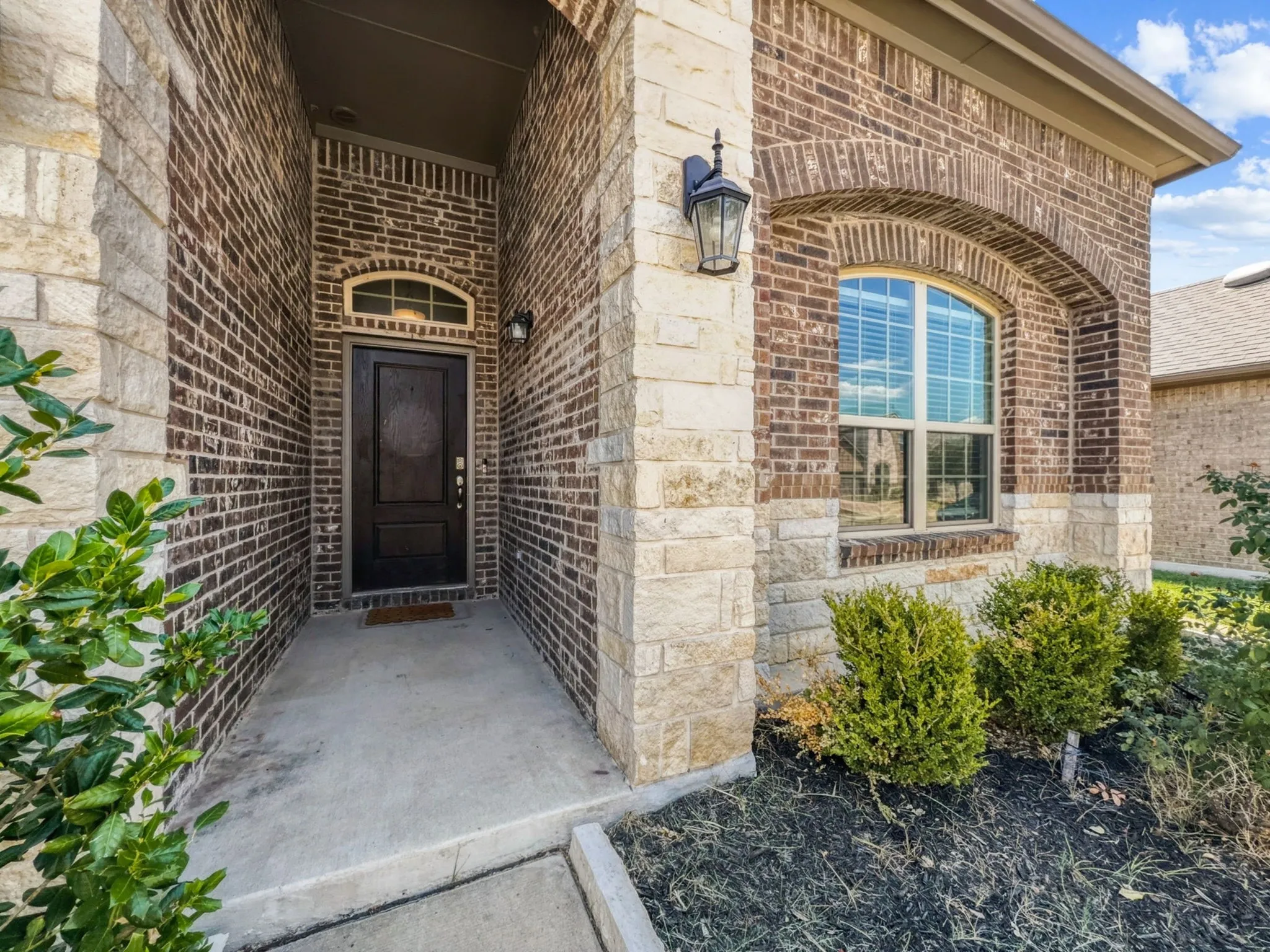 Brick and stone exterior with an arched window and covered entry