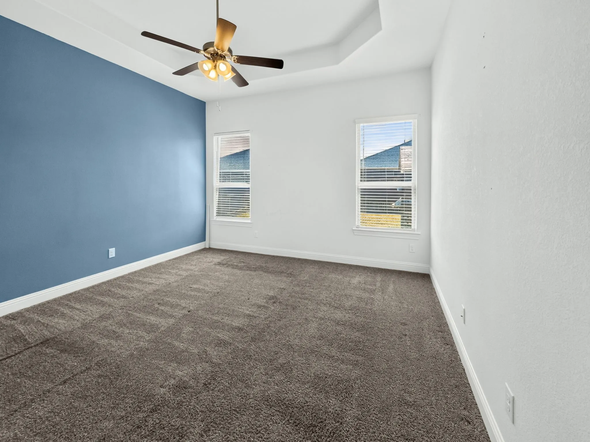 Tray ceiling with a ceiling fan, dual windows with blinds, and textured carpet flooring
